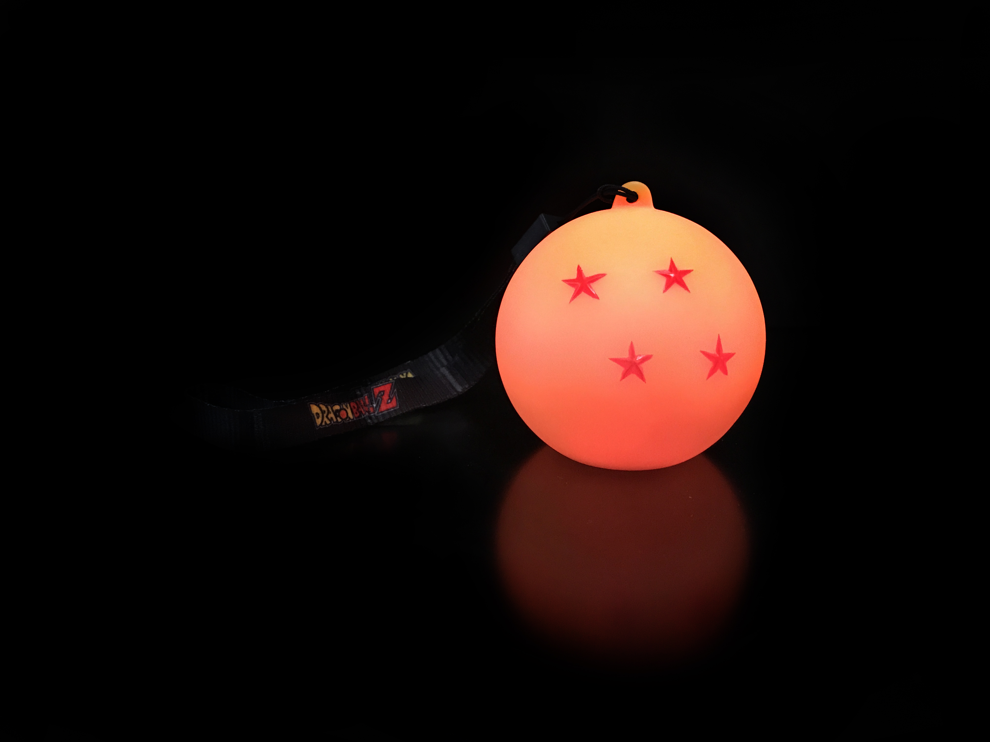 Una sfera del drago arancione brillante con cinque stelle rosse e un cinturino nero su una superficie nera riflettente.