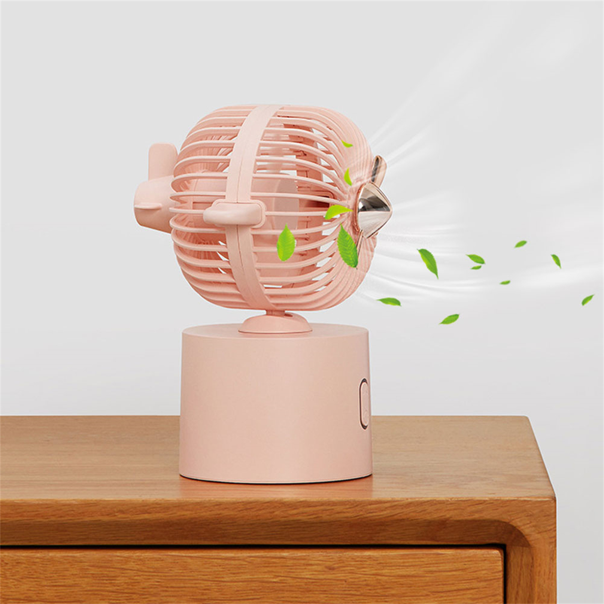 Rosa Ventilator, der Luft mit Blättern auf einem Tisch bläst, heller Hintergrund.