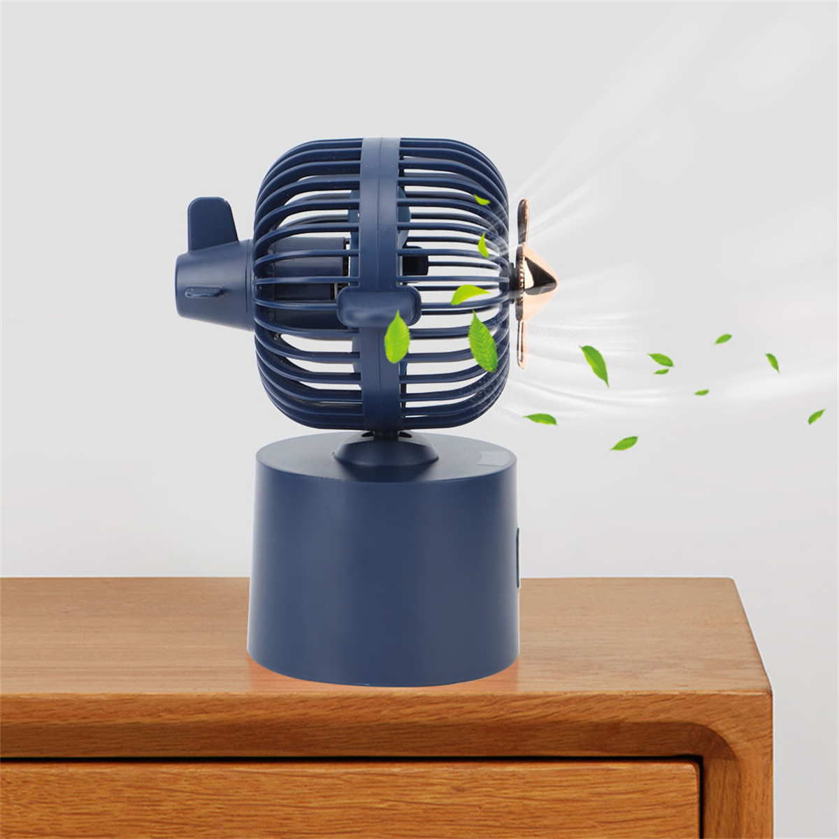 Blauer Schreibtischventilator mit propellerartigem Design. Luft bläst heraus. Blätter und ein Holztisch sichtbar.