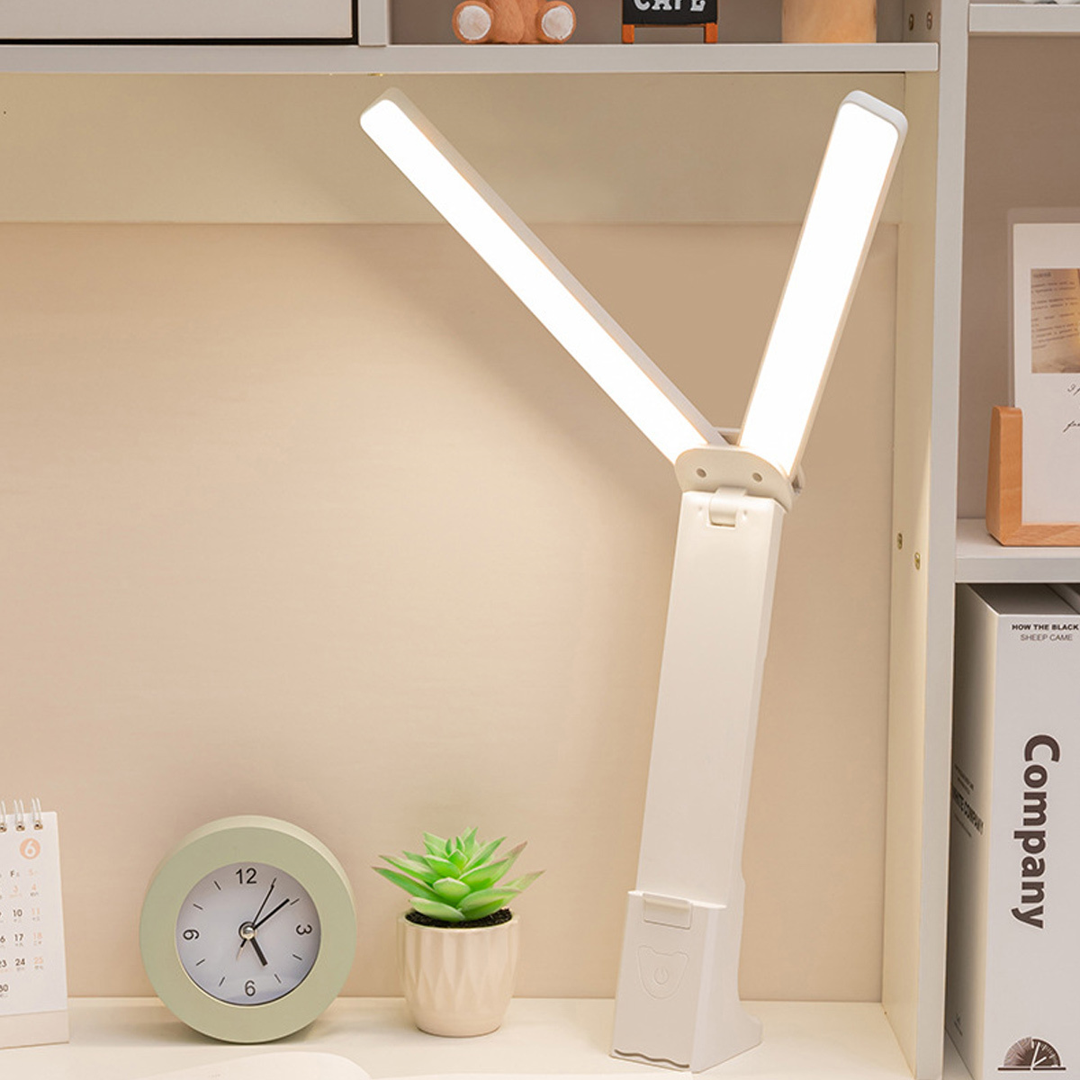 Weiße Schreibtischlampe mit zwei Leuchtpaneelen. Sie steht auf einem Schreibtisch mit Gegenständen im Hintergrund.
