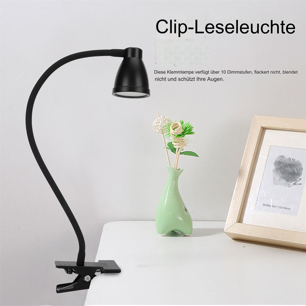 Schwarze Klemm-Leselampe auf einem weißen Tisch. Eine Vase mit dekorativen Blumen und ein Bilderrahmen.