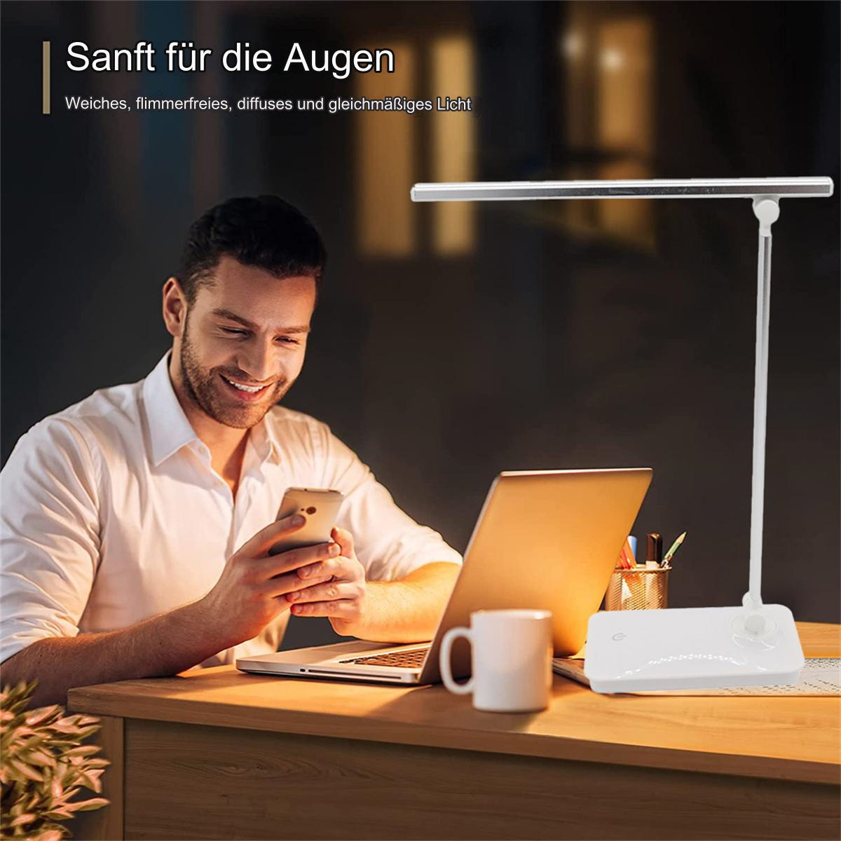 Mann benutzt Handy, Laptop, Lampe und Kaffeetasse auf Schreibtisch.