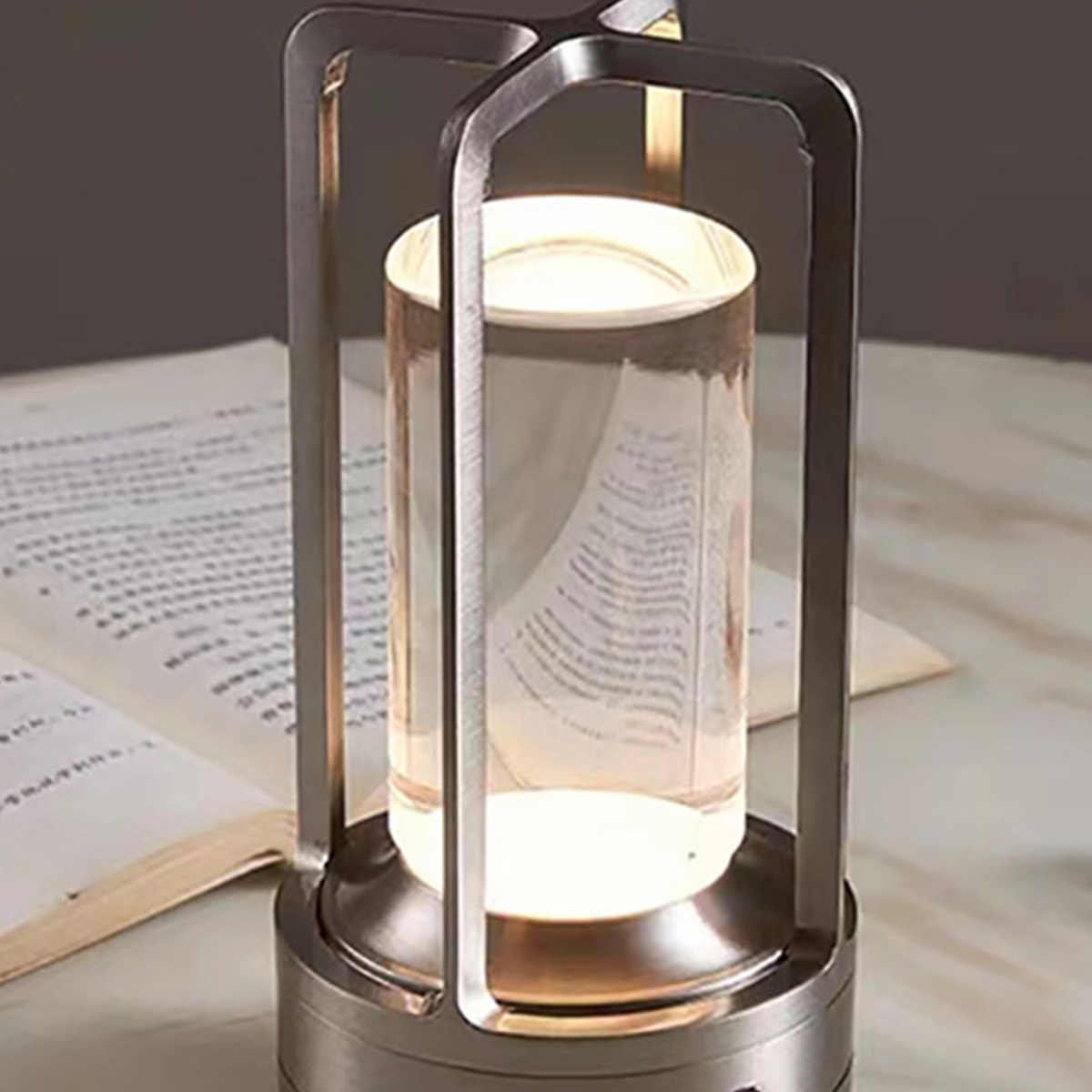 Silber- und Glaslampe auf Marmoroberfläche, mit offenem Buch im Hintergrund.