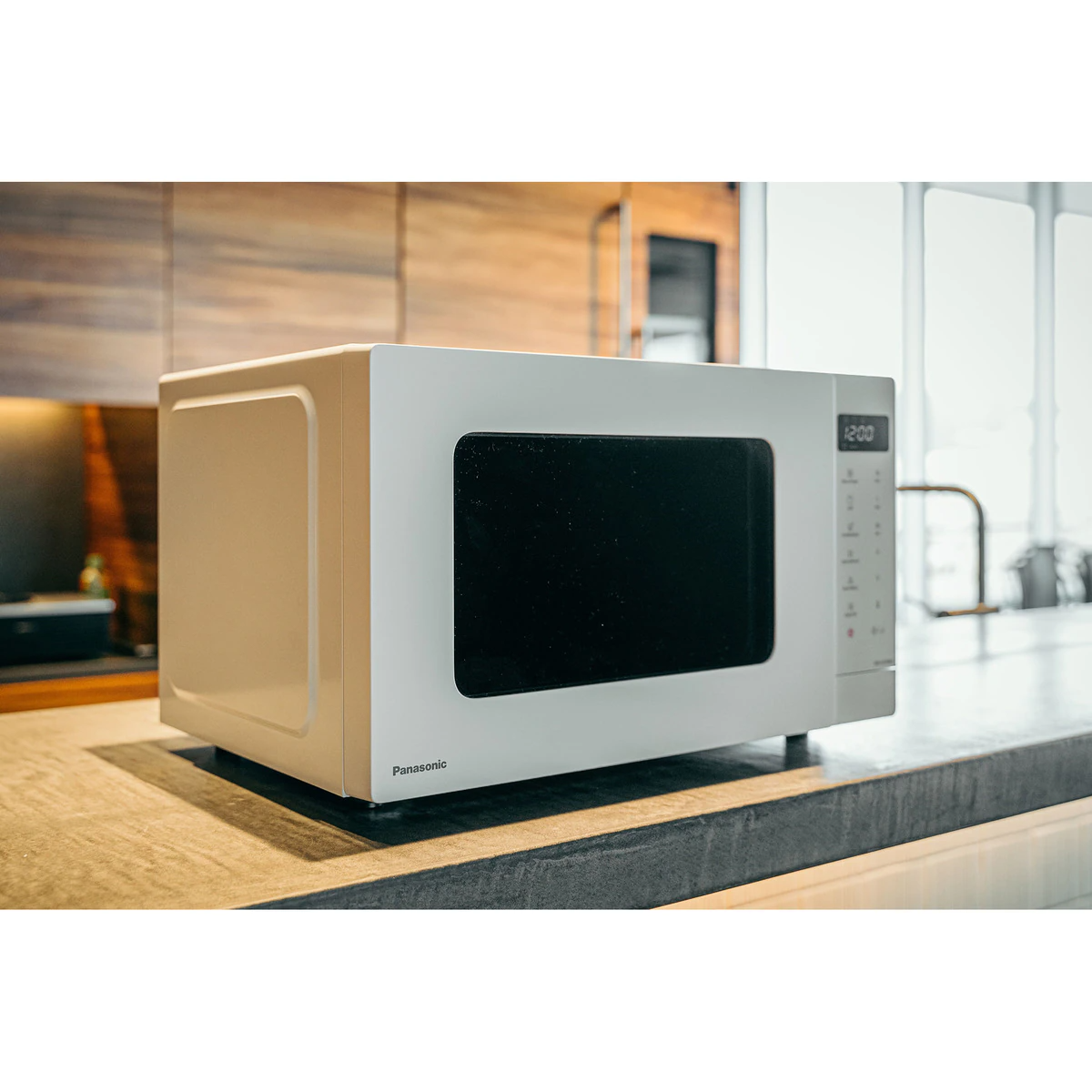 Biała kuchenka mikrofalowa na blacie. Szafki kuchenne i okno w tle.