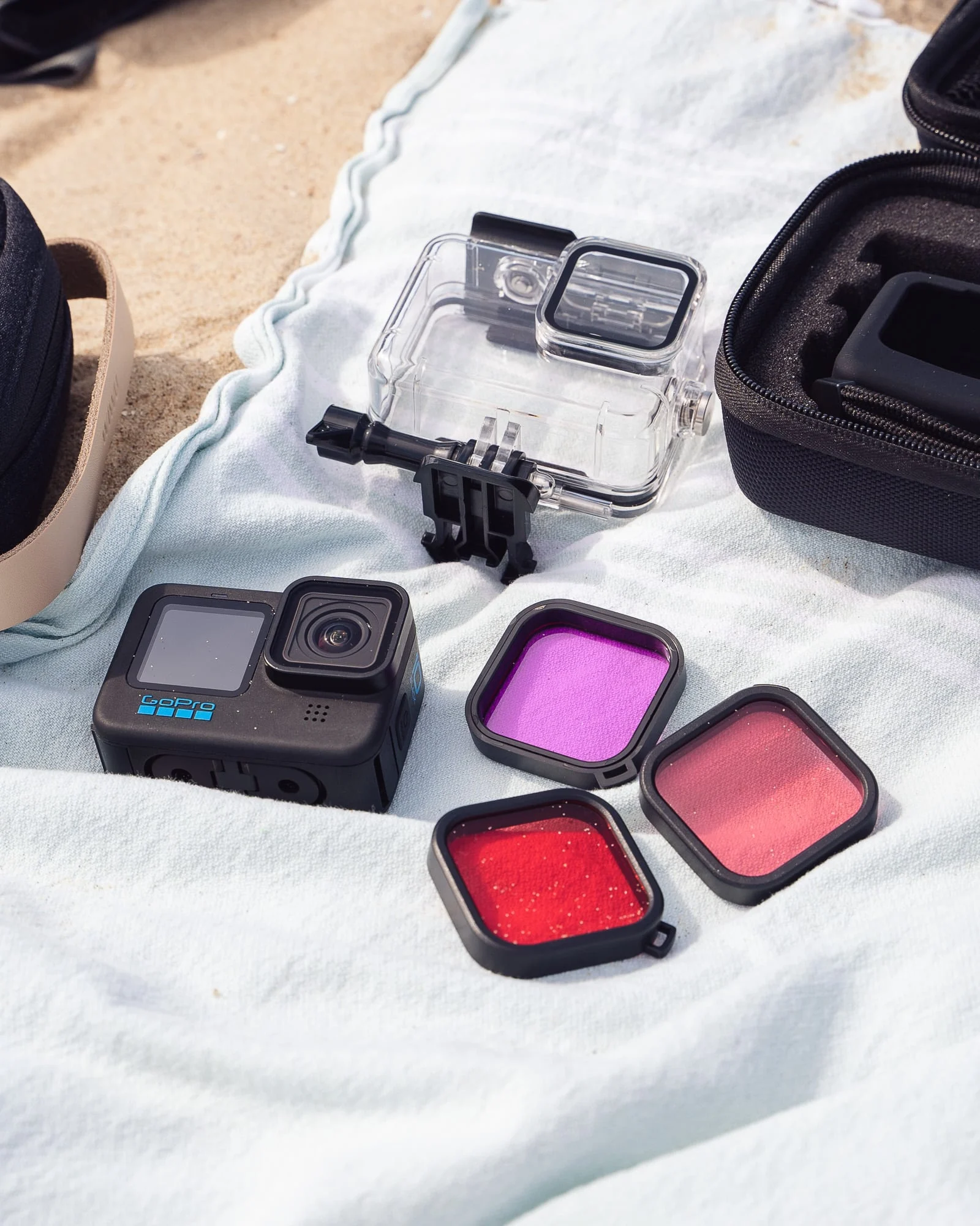 Een GoPro-camera, een doorzichtige hoes en drie gekleurde filters op een handdoek op het strand.