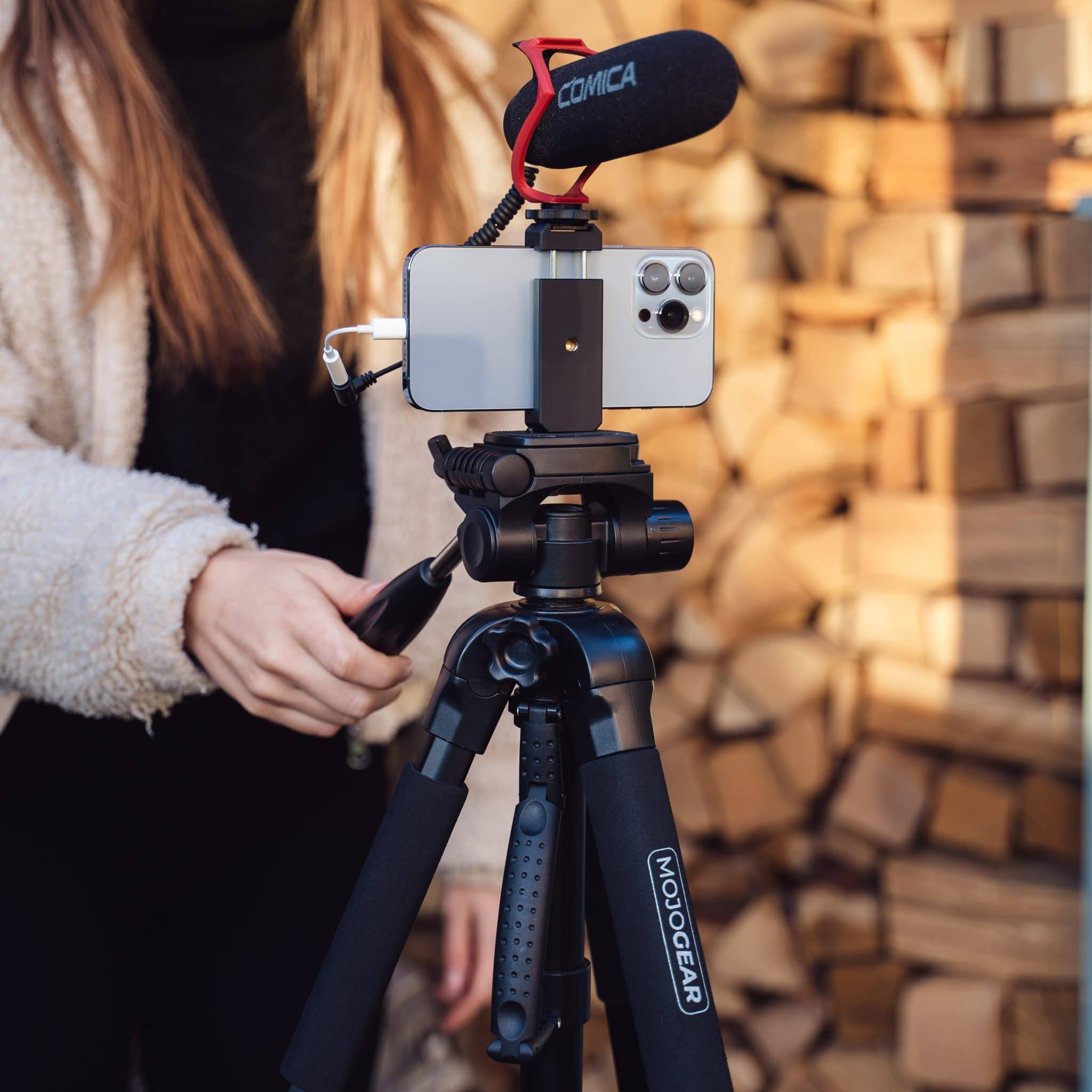 Smartphone on a tripod with a microphone attached, outdoors in front of wood.