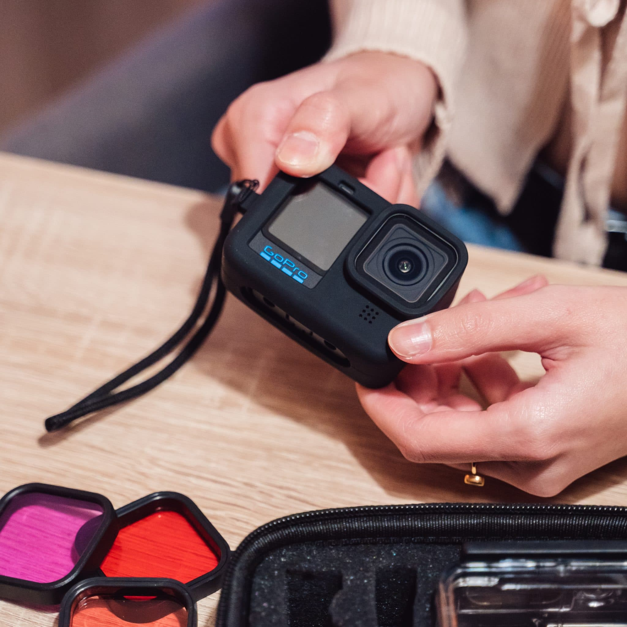Handen die een zwarte GoPro-camera vasthouden. De camera zit in een zwarte hoes.