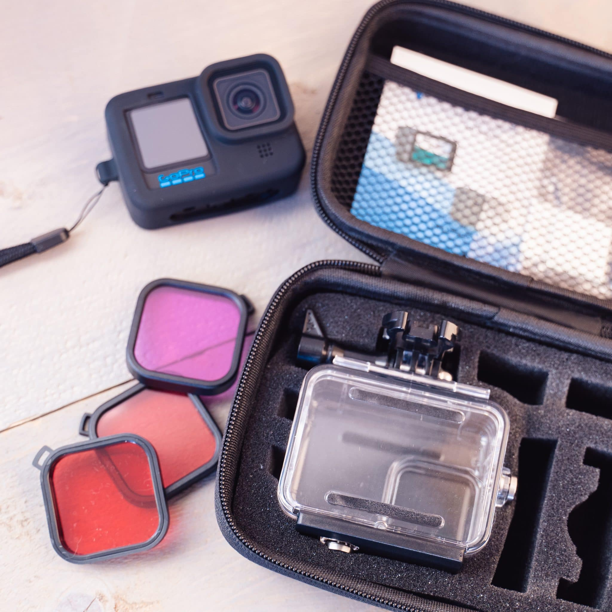 Een zwarte action camera met accessoires: filters, een waterdichte behuizing en een draagtas.