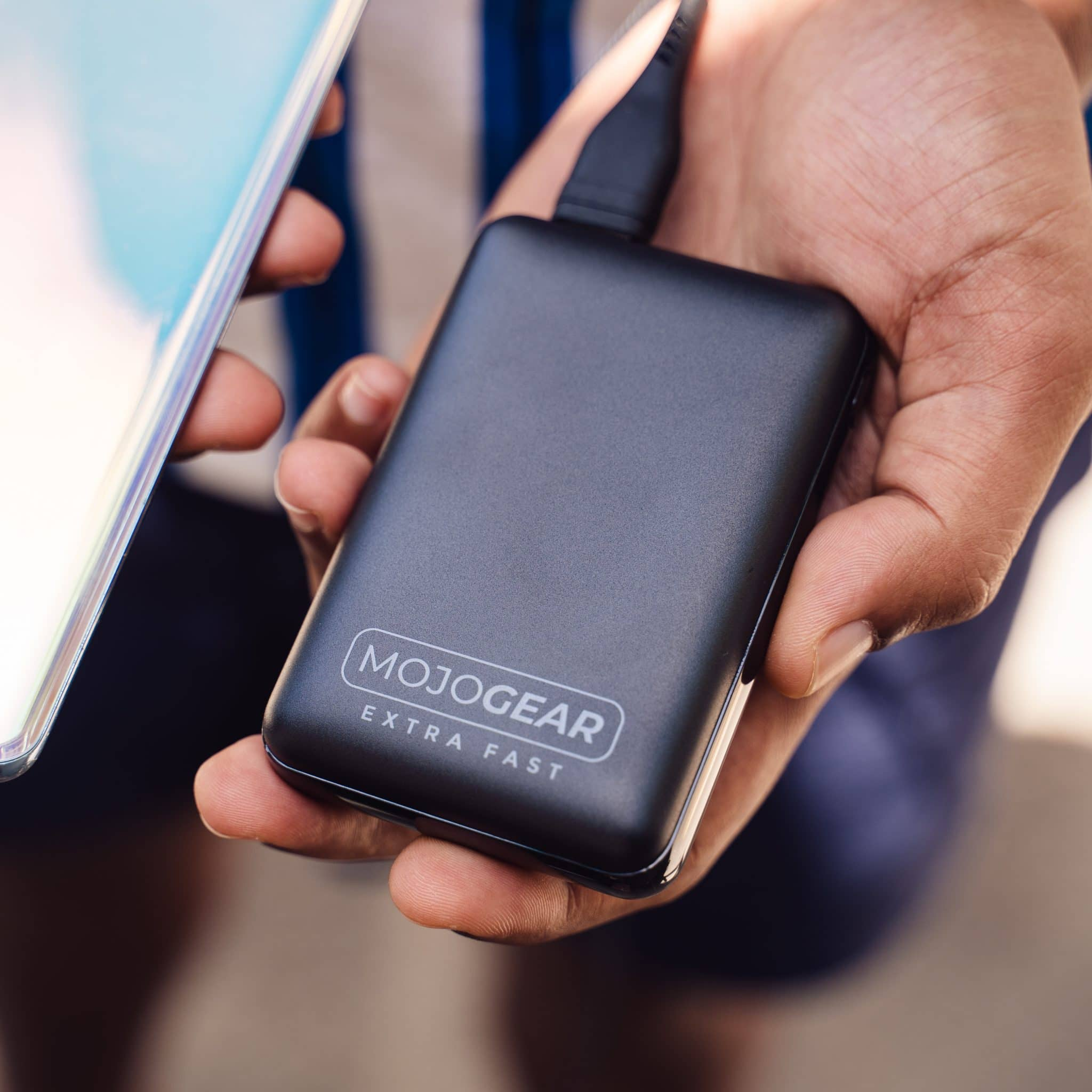 Zwarte draagbare oplader in de hand van een persoon. Een telefoon is zichtbaar aan de linkerkant.