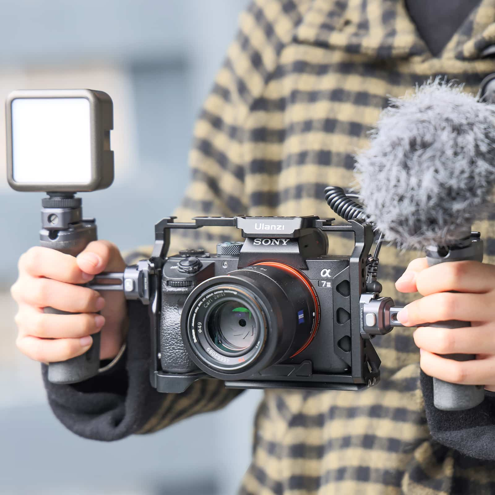 Een persoon die een camera vasthoudt met een licht en microfoon bevestigd. De camera heeft een lens en een kooi.