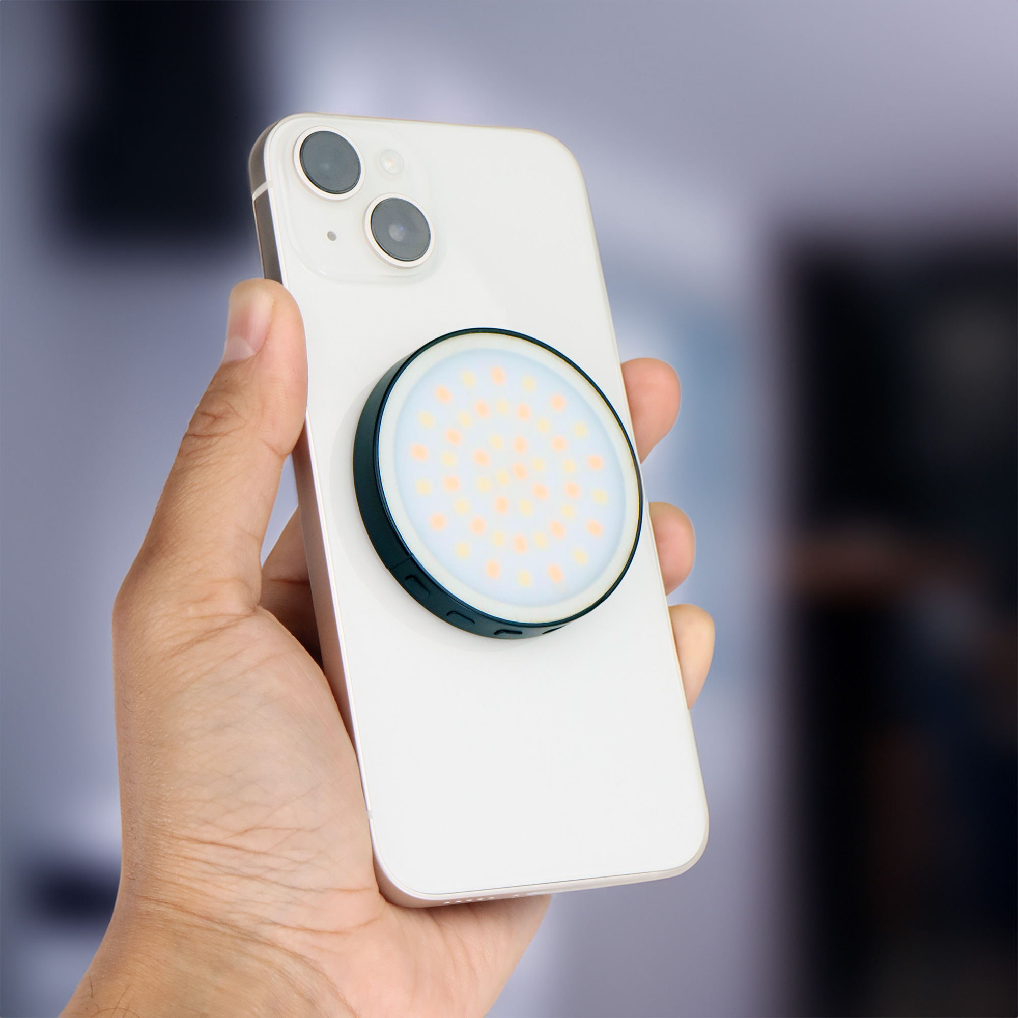 A phone with a round light attachment is held in a hand. The light is on.