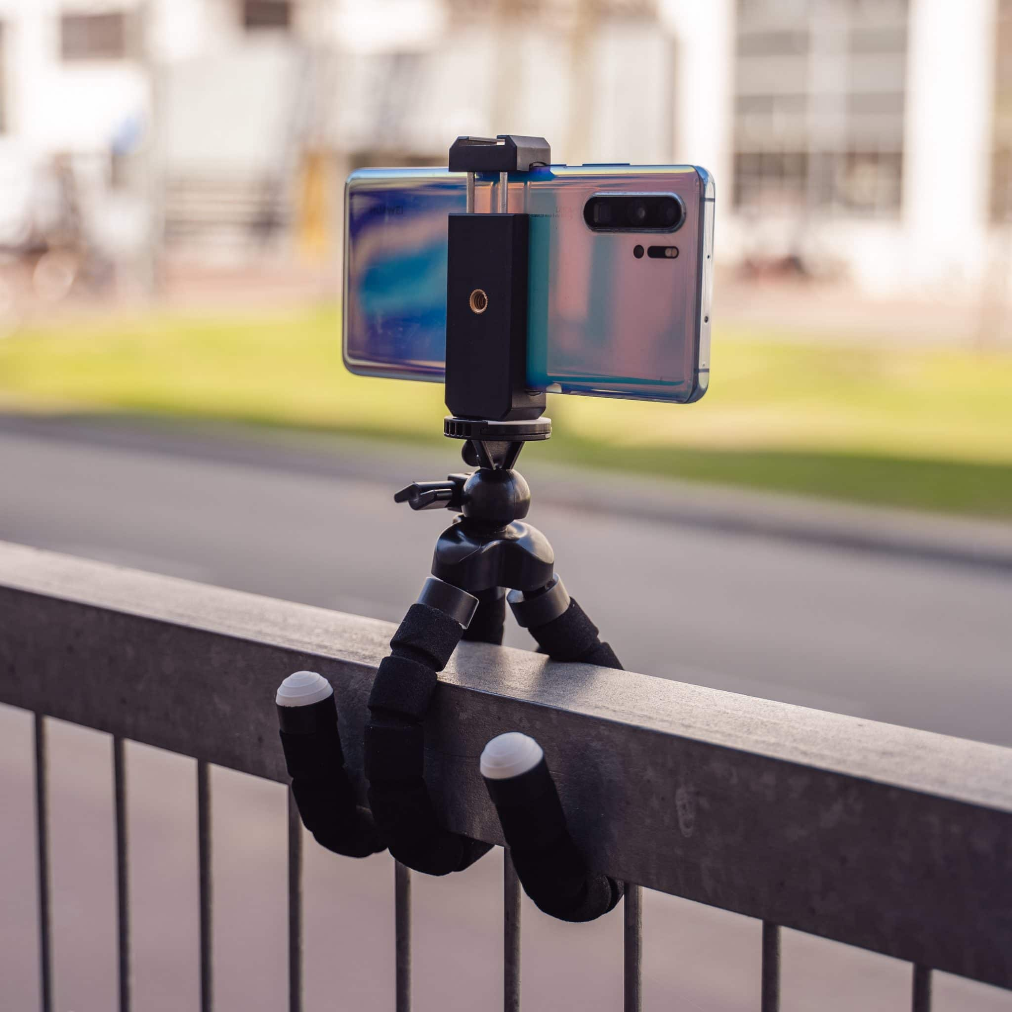 Een telefoon op een flexibel zwart statief, gemonteerd op een metalen reling.