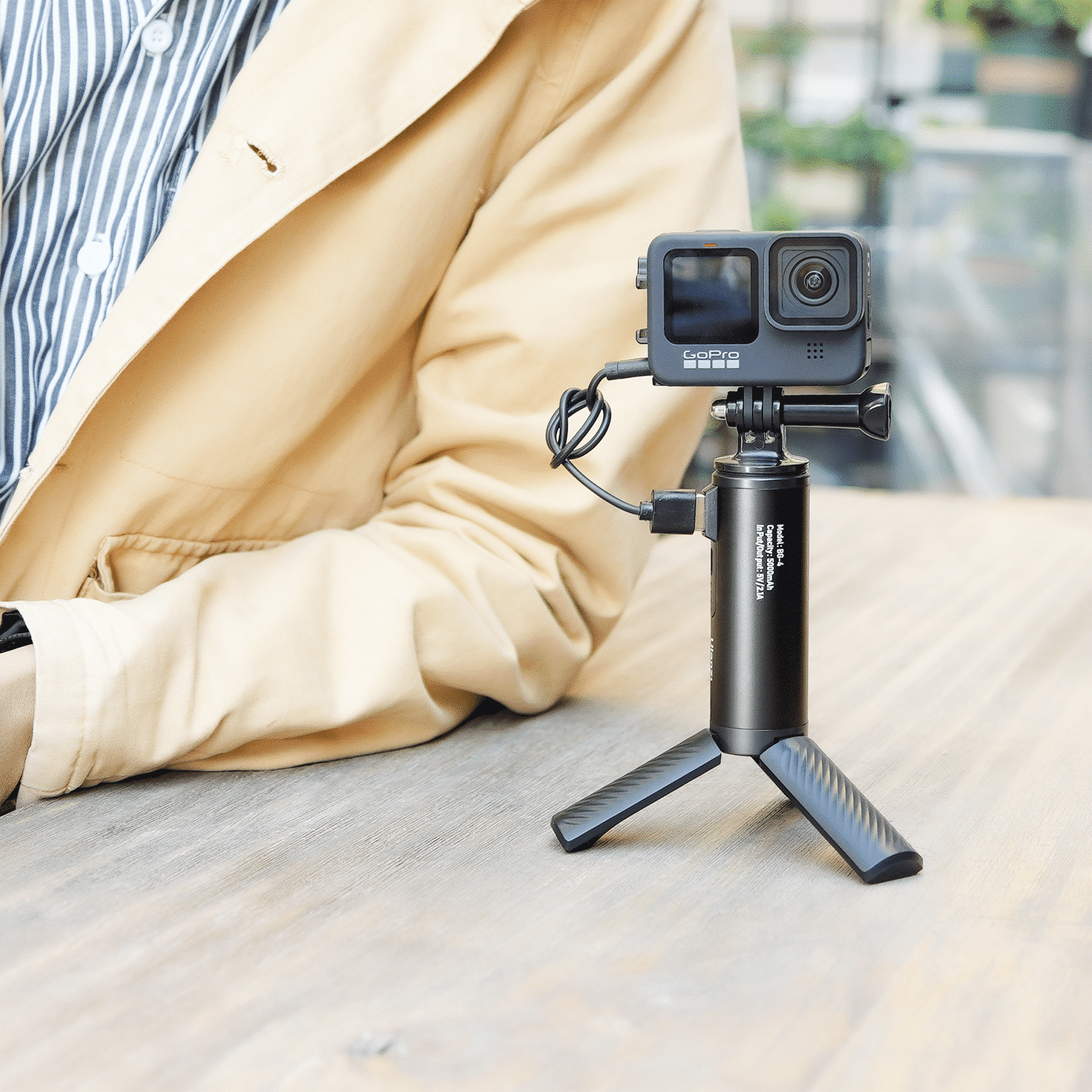 Personne avec caméra GoPro sur trépied. Caméra noire, trépied noir, table en bois.