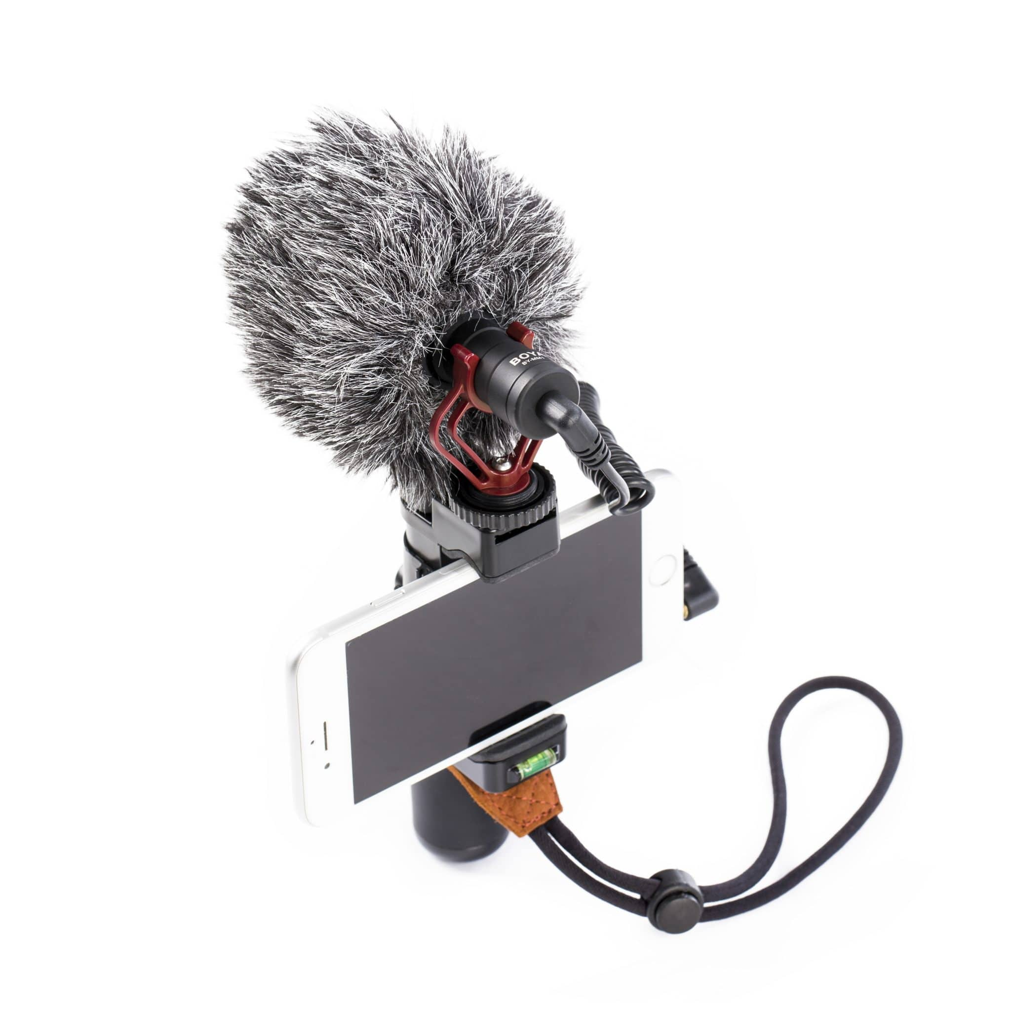 Microphone fixé à un téléphone, monté sur un support, avec une sangle noire. Fond blanc.