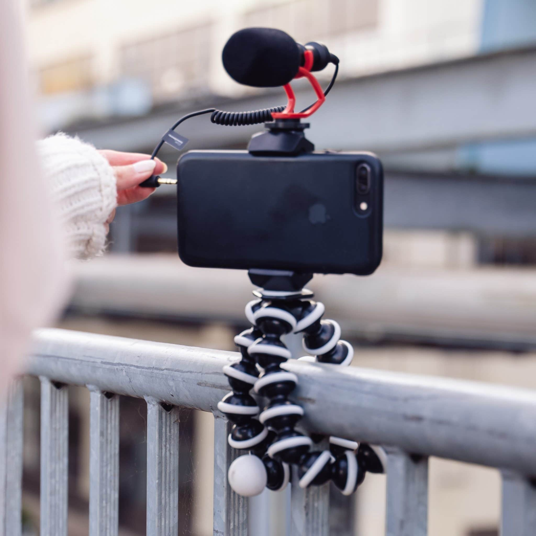 A phone with a microphone attached is mounted on a tripod. A hand is holding the cable.