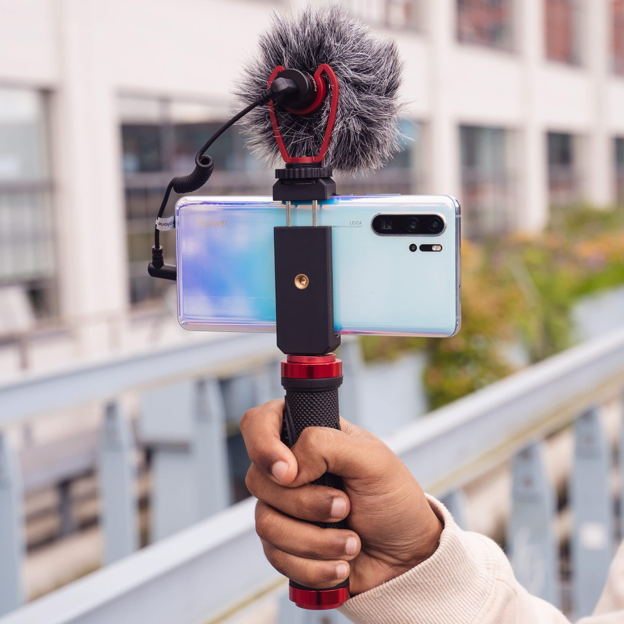 Persoon die een telefoon vasthoudt met een microfoon, met uitzicht op een brug.