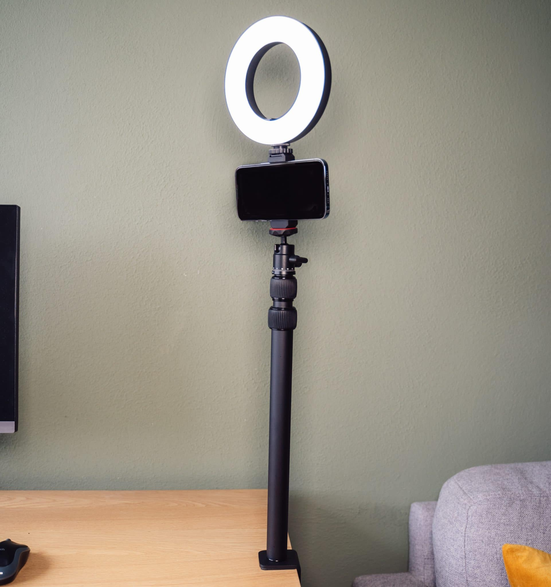 A ring light with a phone attached to it, mounted on a desk clamp.