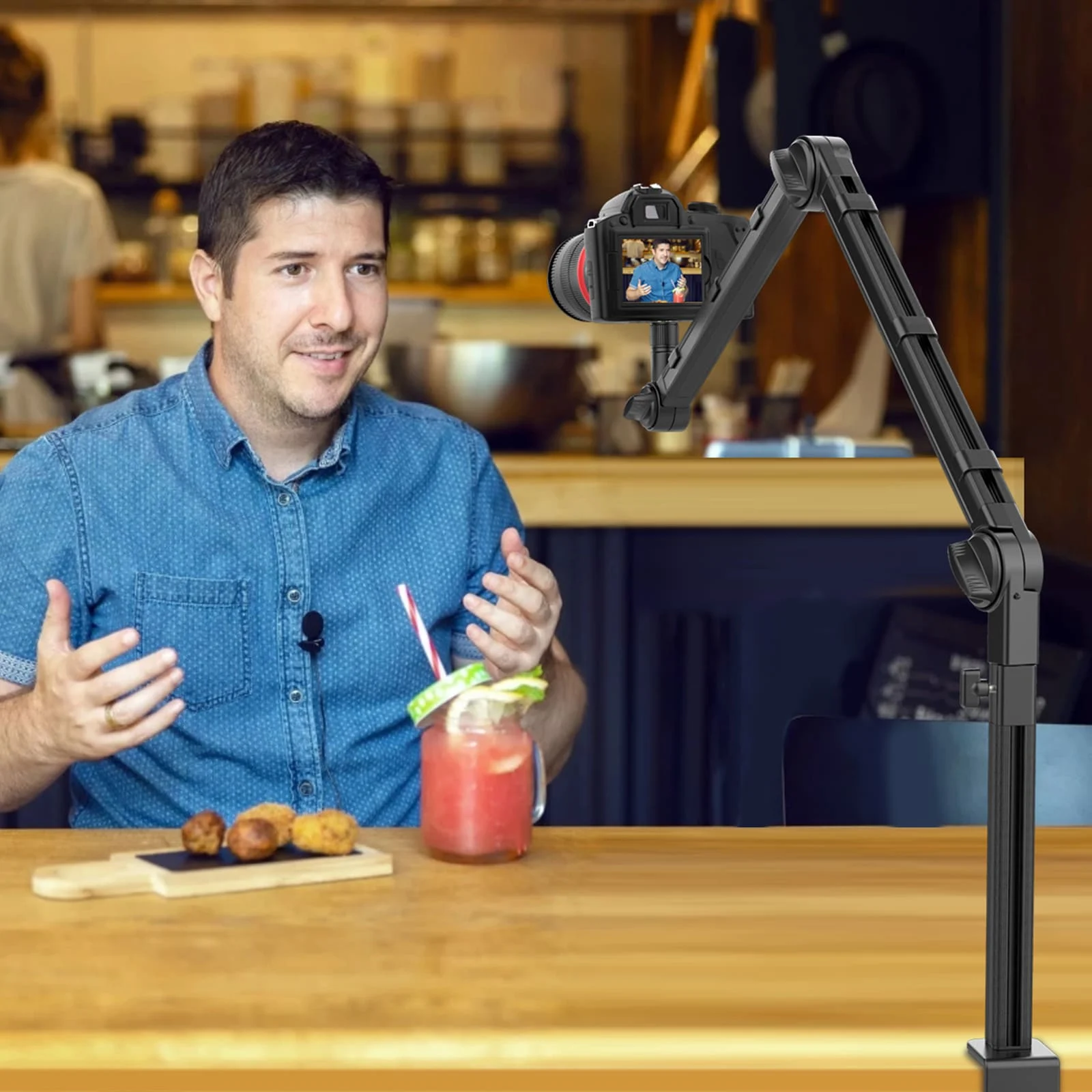 Man filming with a camera on a stand, a drink and food on the table.
