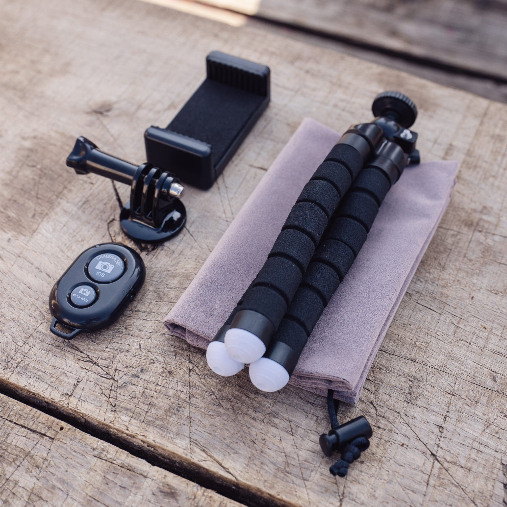 A tripod, phone holder, and remote button are arranged on a wooden surface.