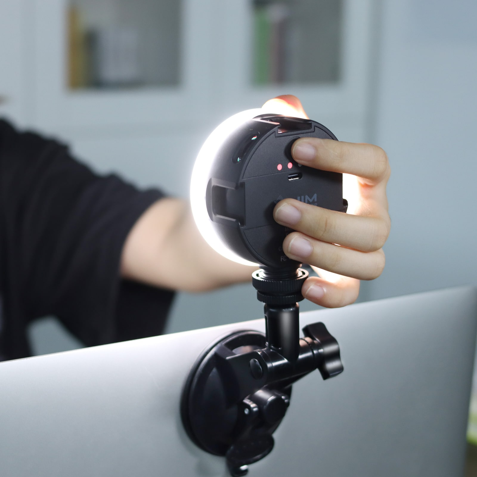 A hand holds a small LED light. It's mounted on a laptop. The light is on.