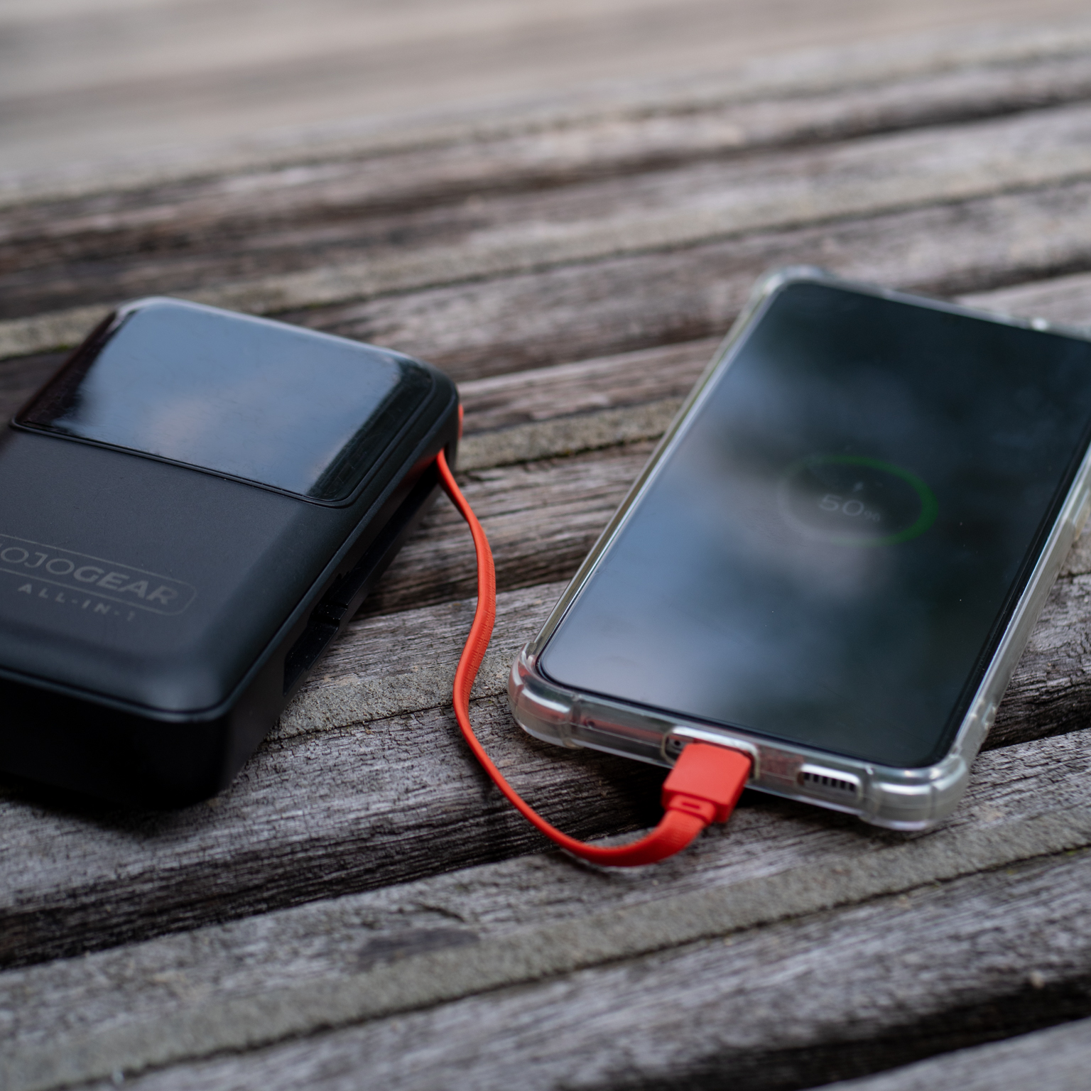 Zwarte powerbank die een smartphone oplaadt met een oranje kabel. Houten oppervlak.