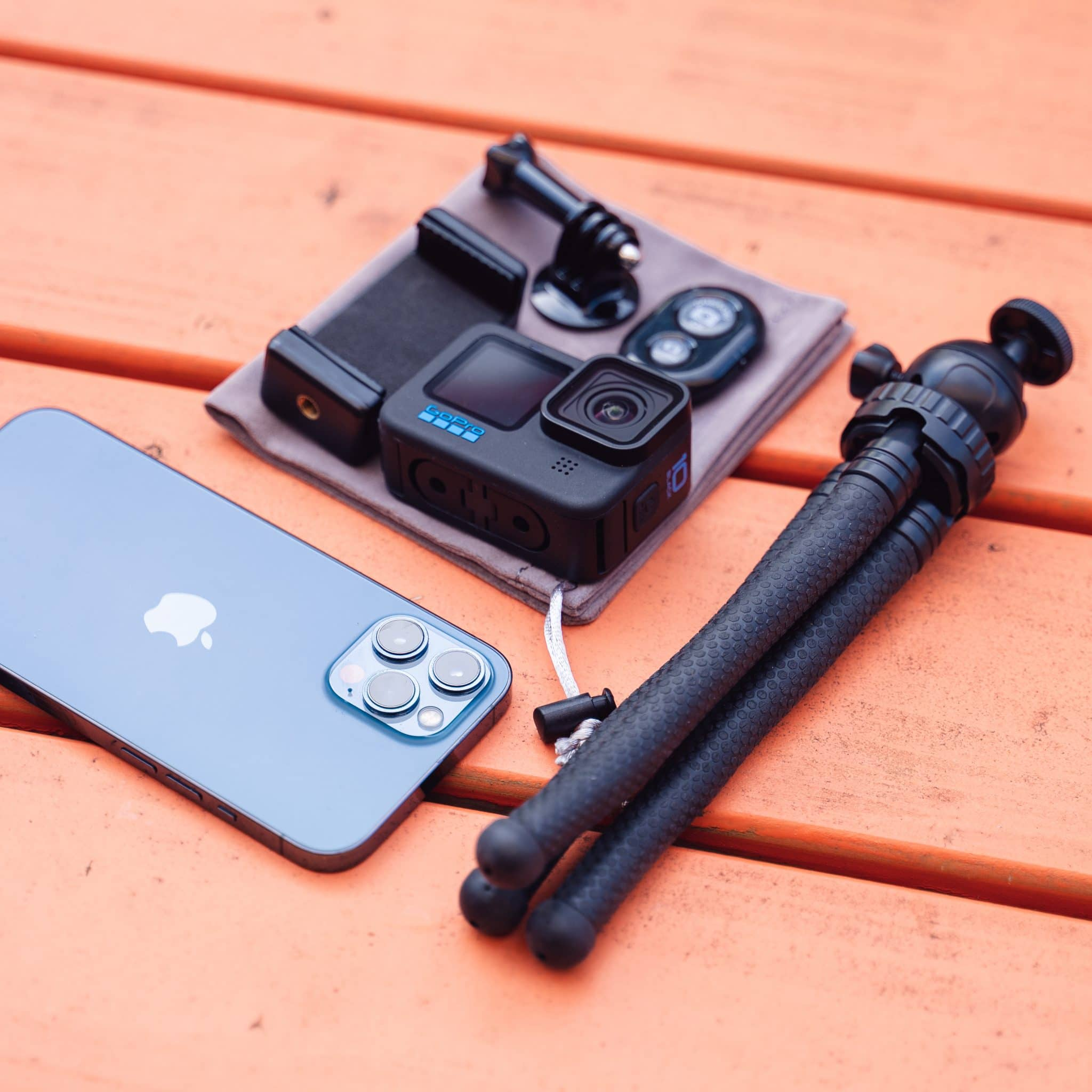 GoPro, blue phone, small tripod, and accessories on an orange wooden surface.