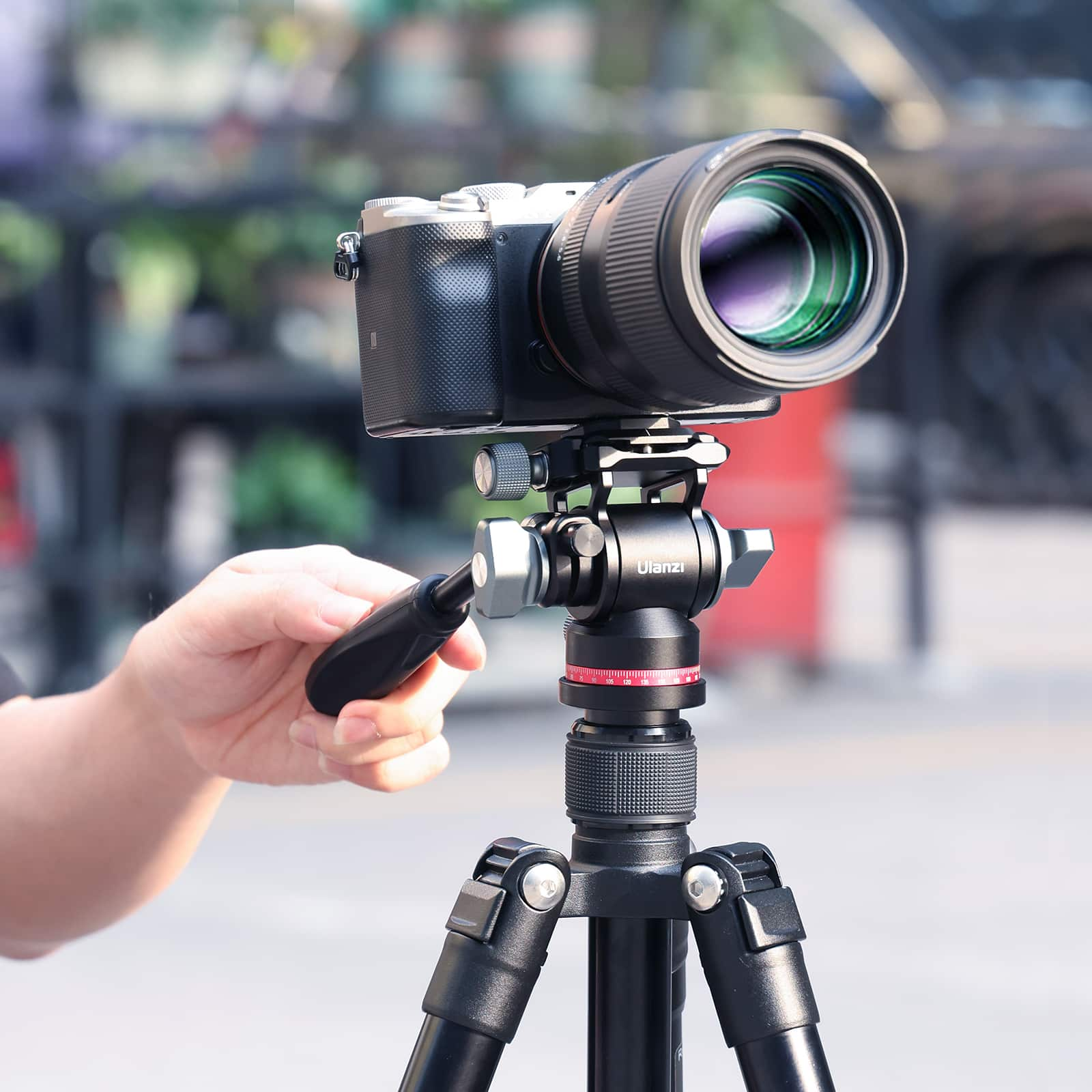 Aparat na statywie, trzymany przez rękę. Aparat ma duży obiektyw i czarny korpus.