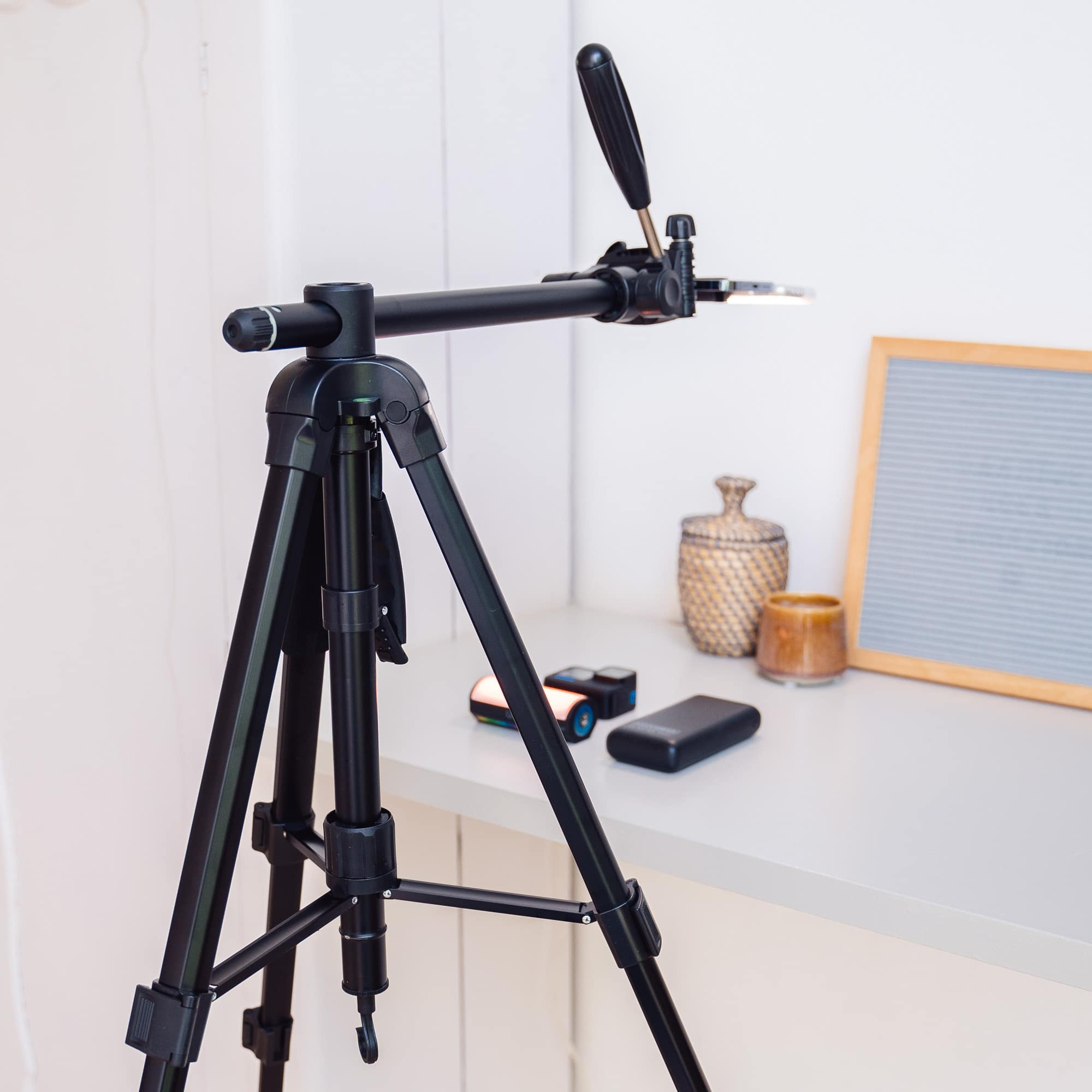 A black tripod with a phone holder is on a table, with other items on the table.