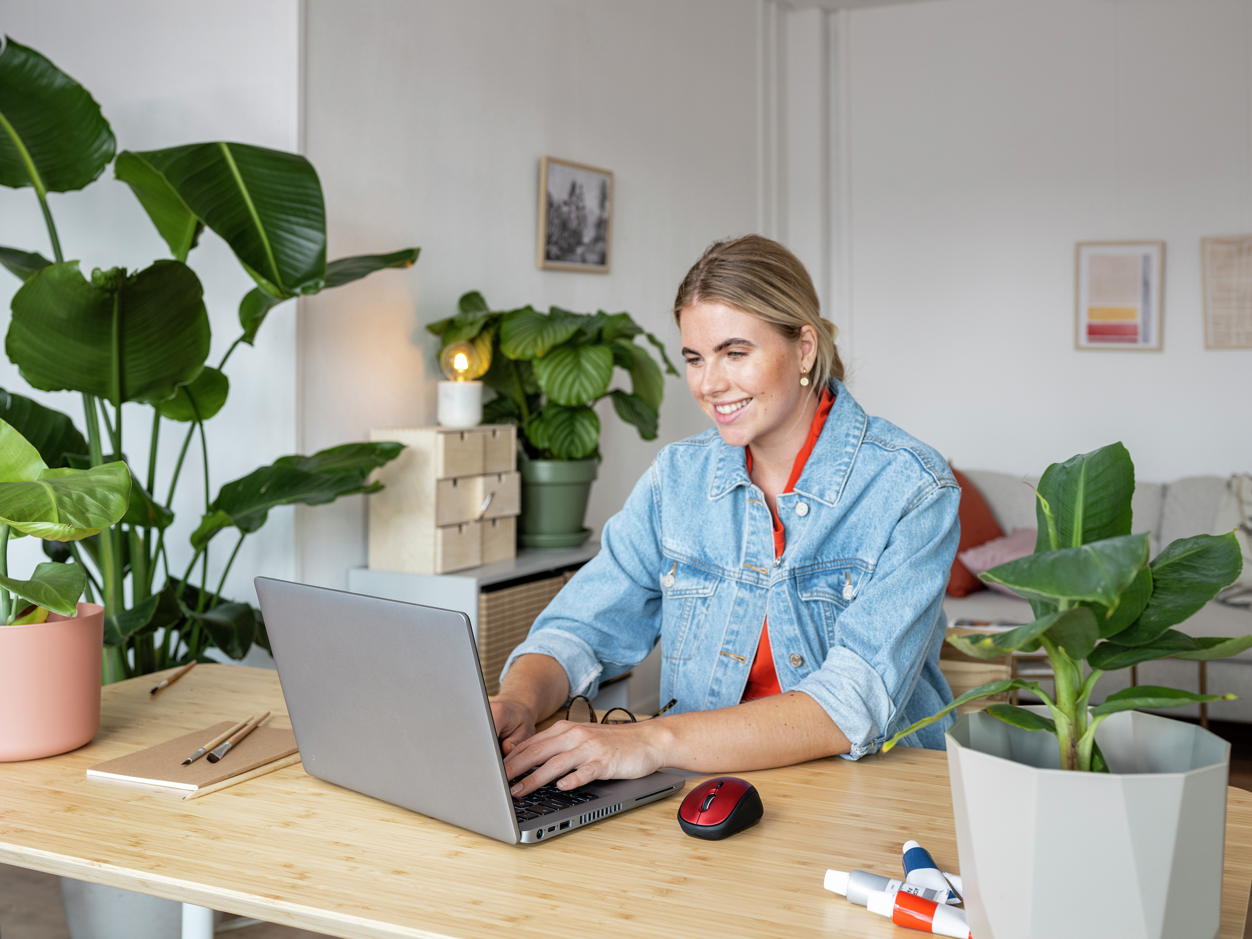 Blondynka uśmiecha się, pracując na laptopie przy drewnianym biurku.