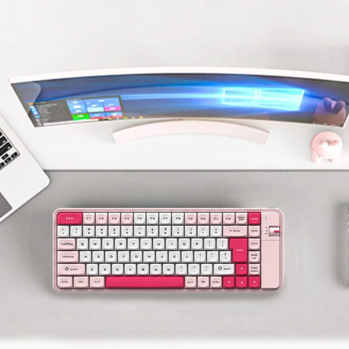 Eine rosa Tastatur auf einem Schreibtisch mit einem Monitor und einem rosa Schwein. Die Tastatur hat weiße Tasten und rotes Enter.