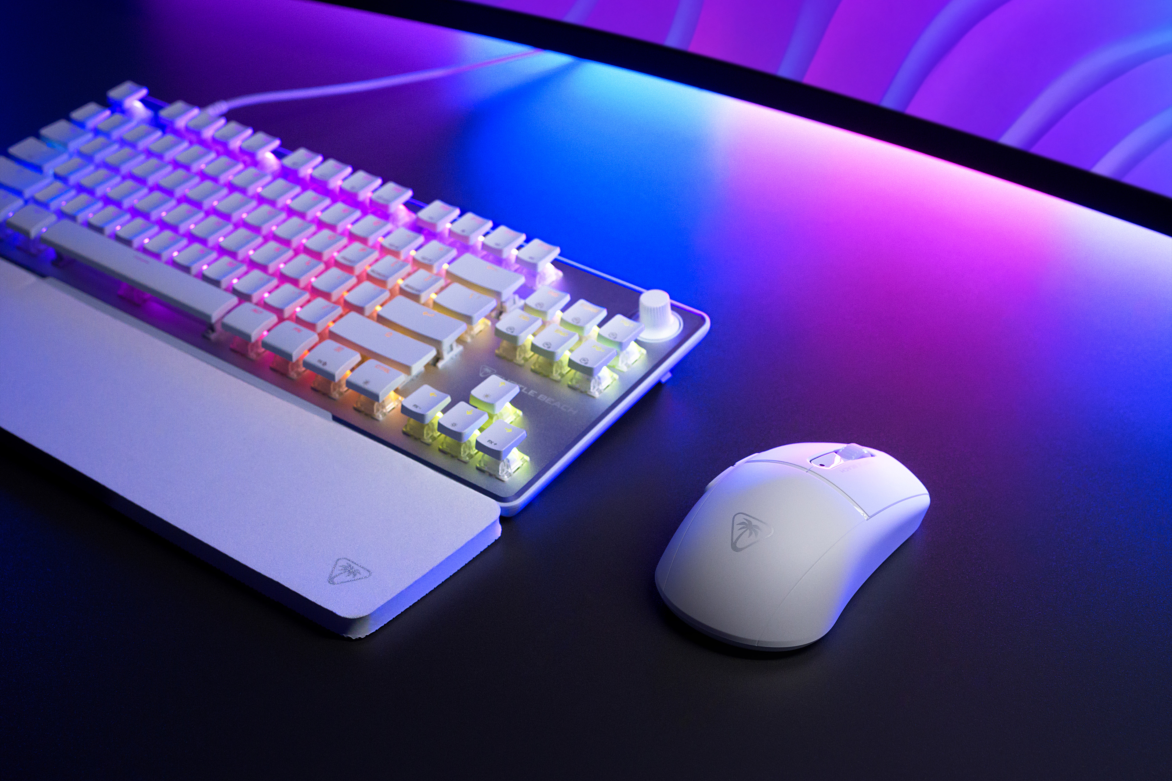 Biała klawiatura i mysz na ciemnej powierzchni. Kolorowy ekran w tle.