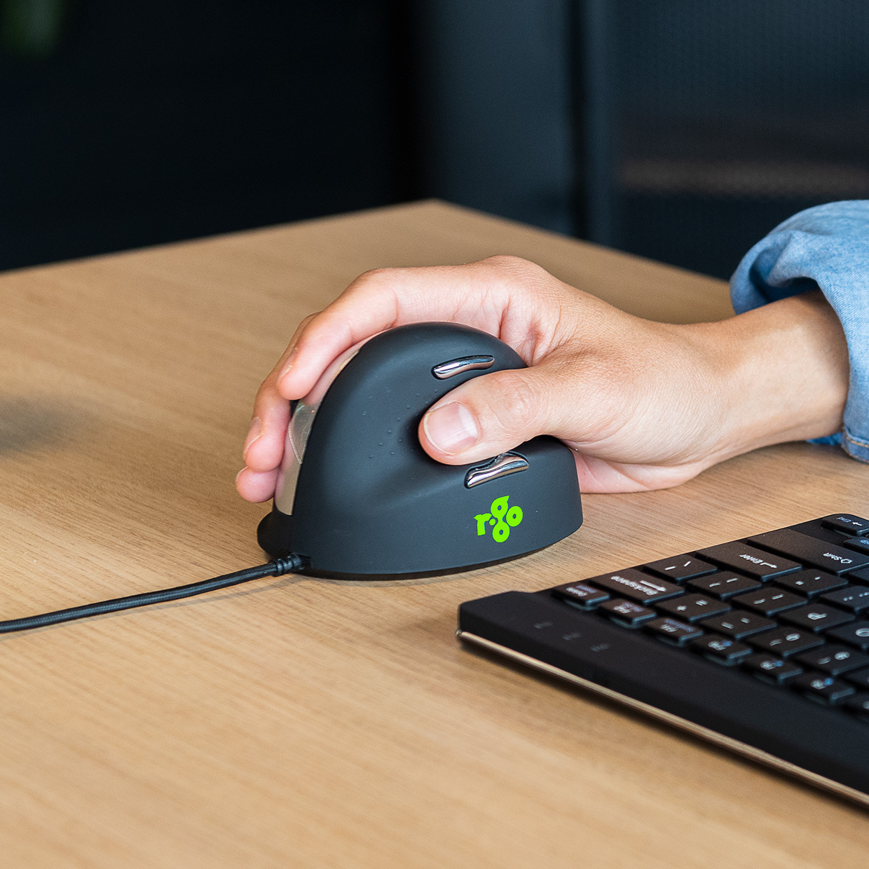 Hand einer Person, die eine vertikale ergonomische Maus auf einem Holzschreibtisch benutzt.