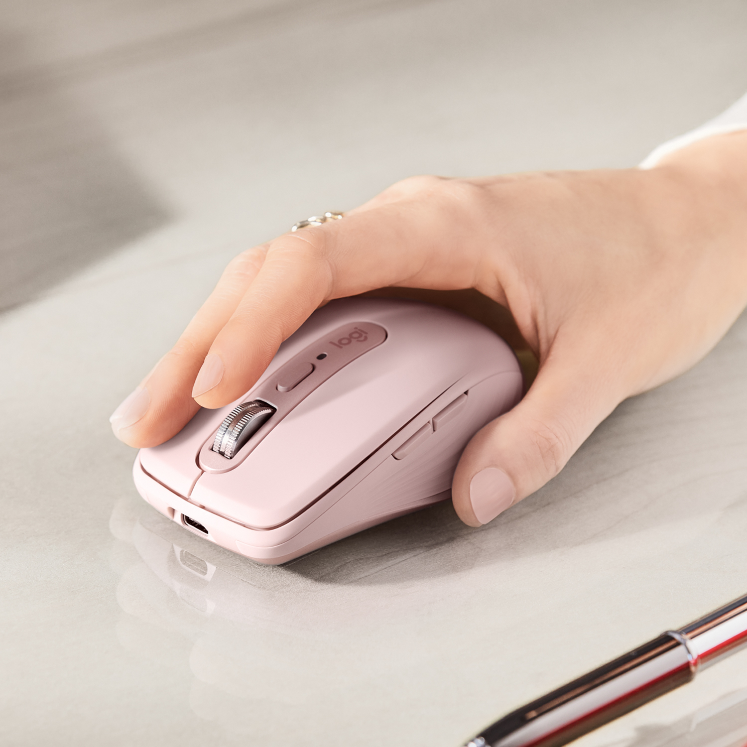 La mano di una persona che usa un mouse wireless rosa su una superficie grigio chiaro. Il mouse ha una rotella.