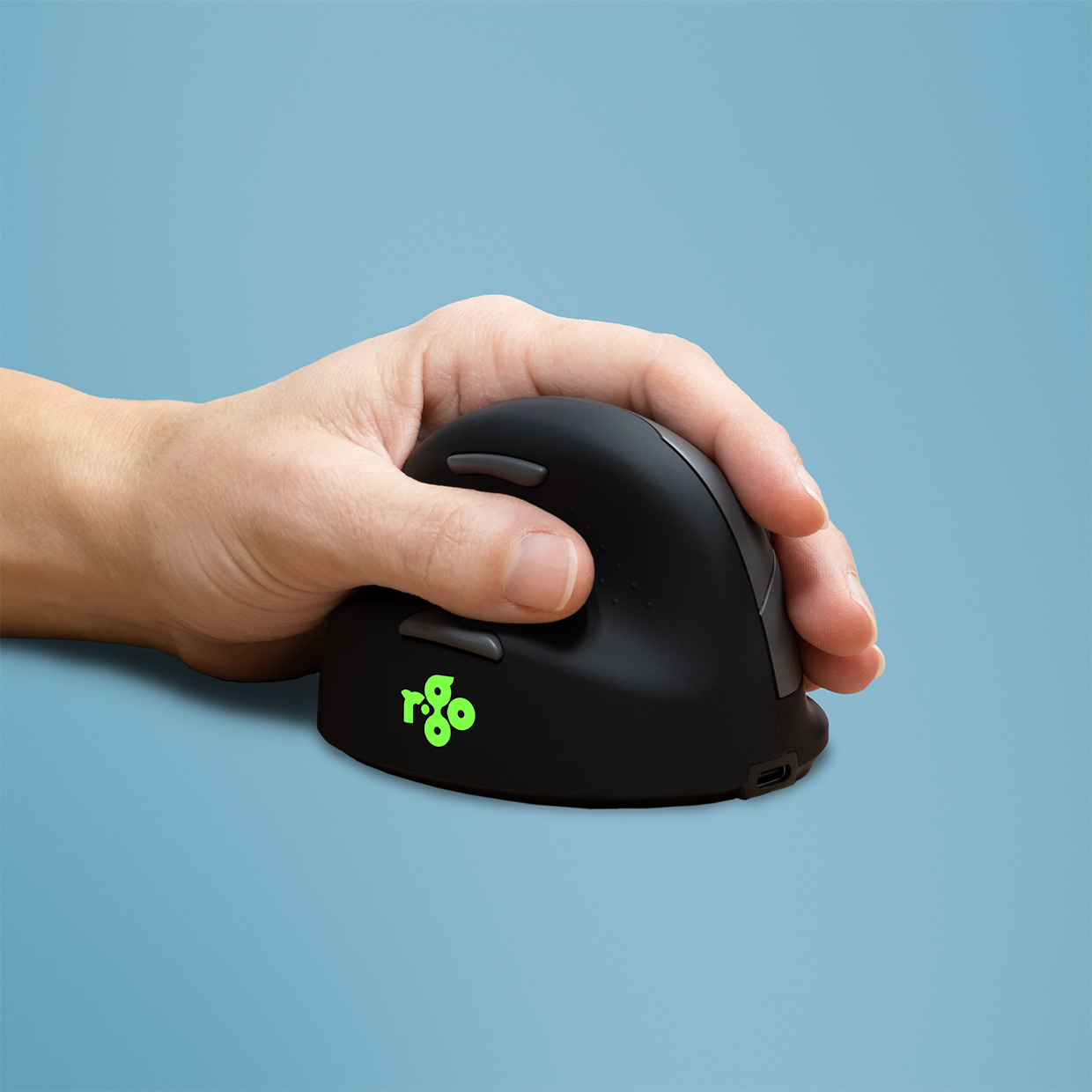 Hand hält eine schwarze ergonomische Maus. Die Maus hat ein grün leuchtendes Logo.