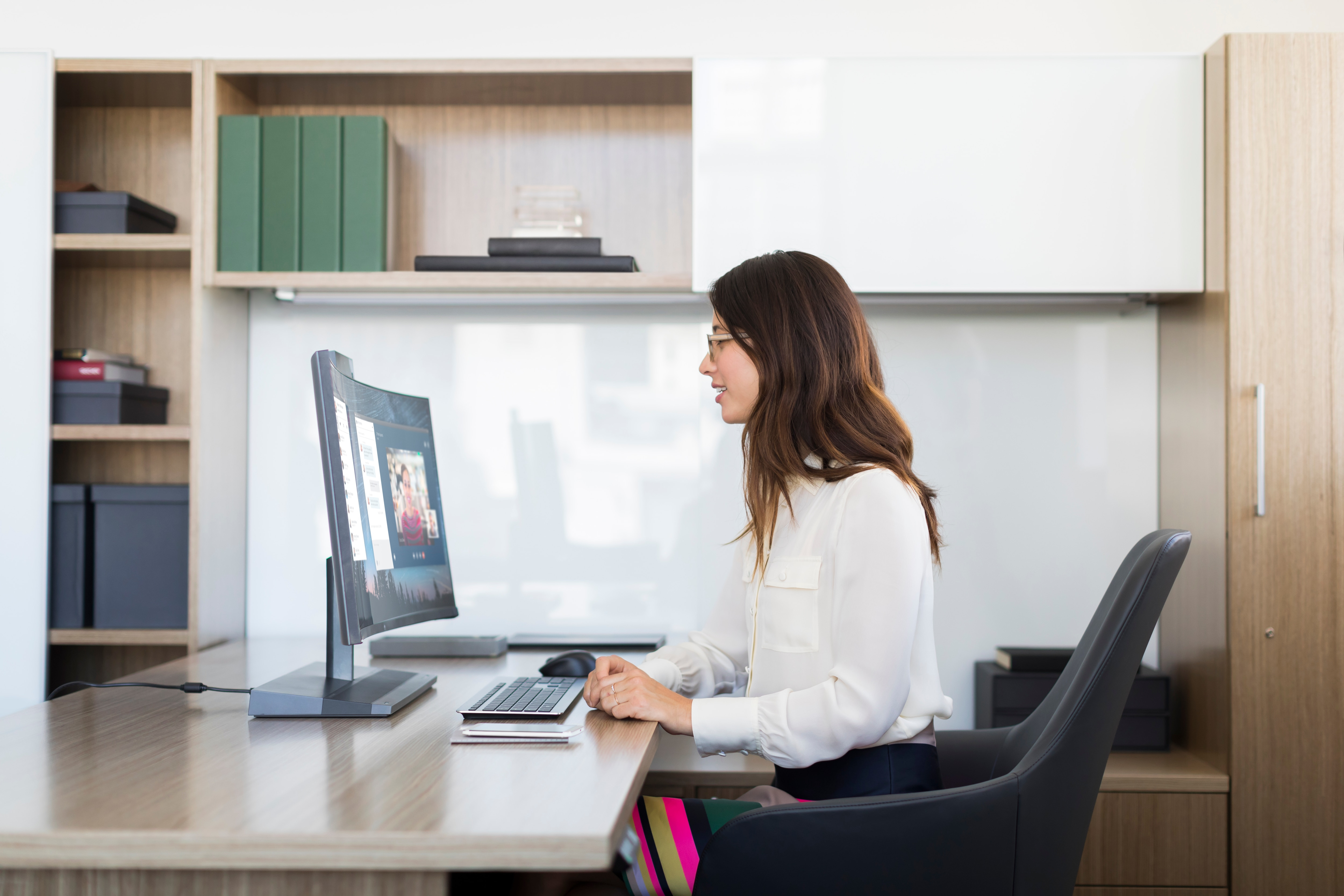 Kobieta w białej koszuli siedzi przy biurku z monitorem. Jest w biurze.