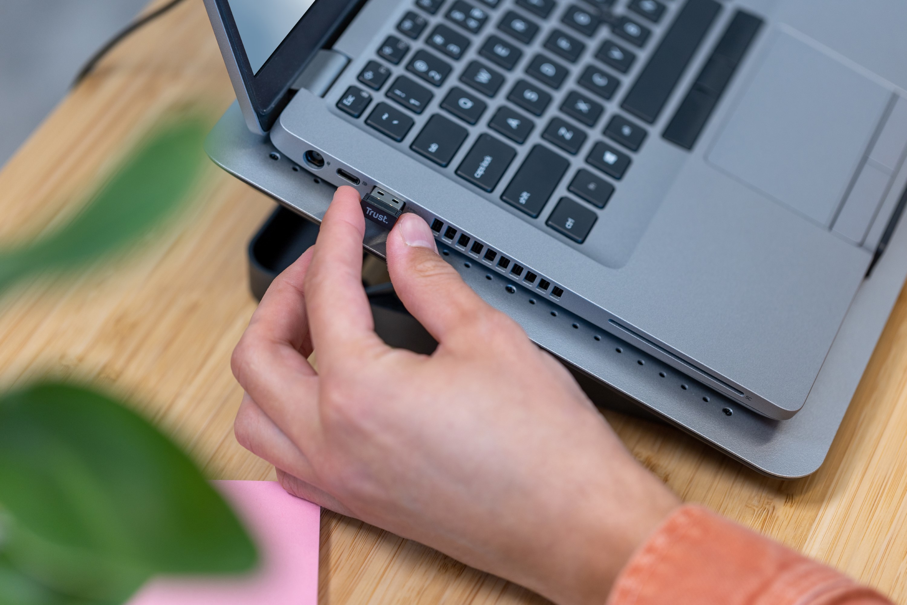 Main insère un récepteur USB dans un ordinateur portable, bureau en bois et post-it en vue.