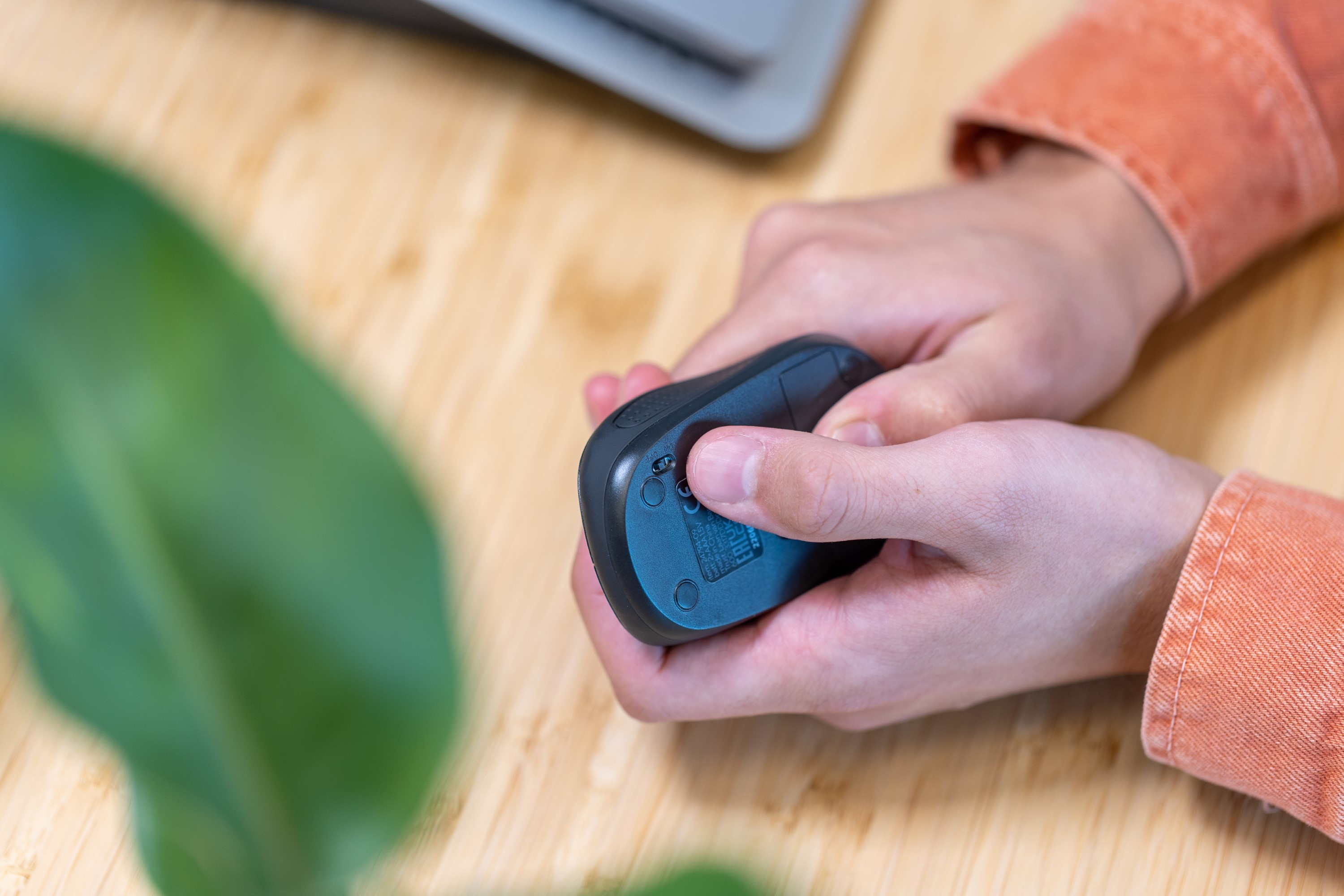 Mains tenant une souris ergonomique noire, avec une feuille au premier plan.