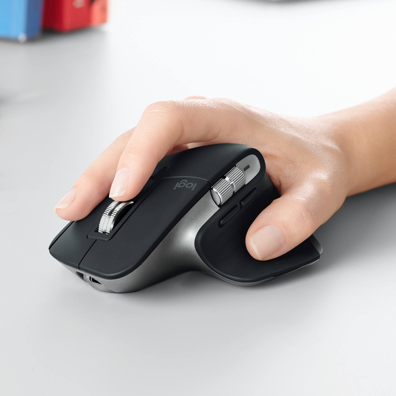 Mano che usa un mouse Logitech nero e argento su una superficie grigia.