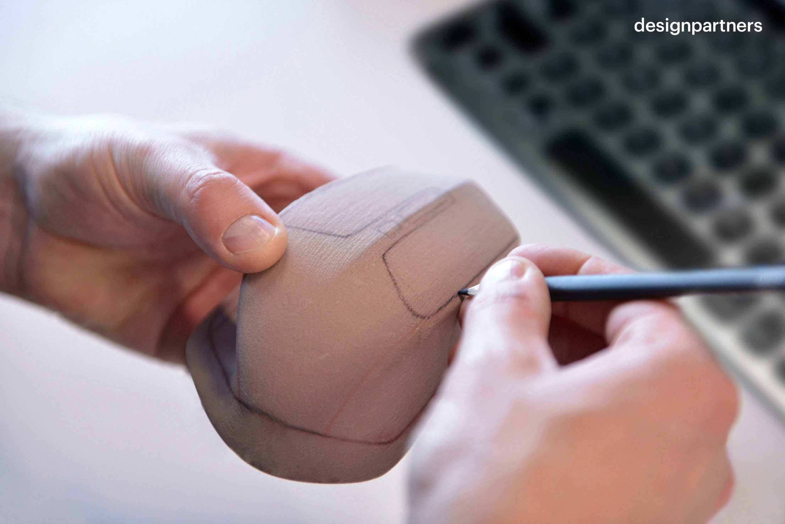 Ręce szkicują projekt myszy na jasnobrązowym modelu z klawiaturą w tle.