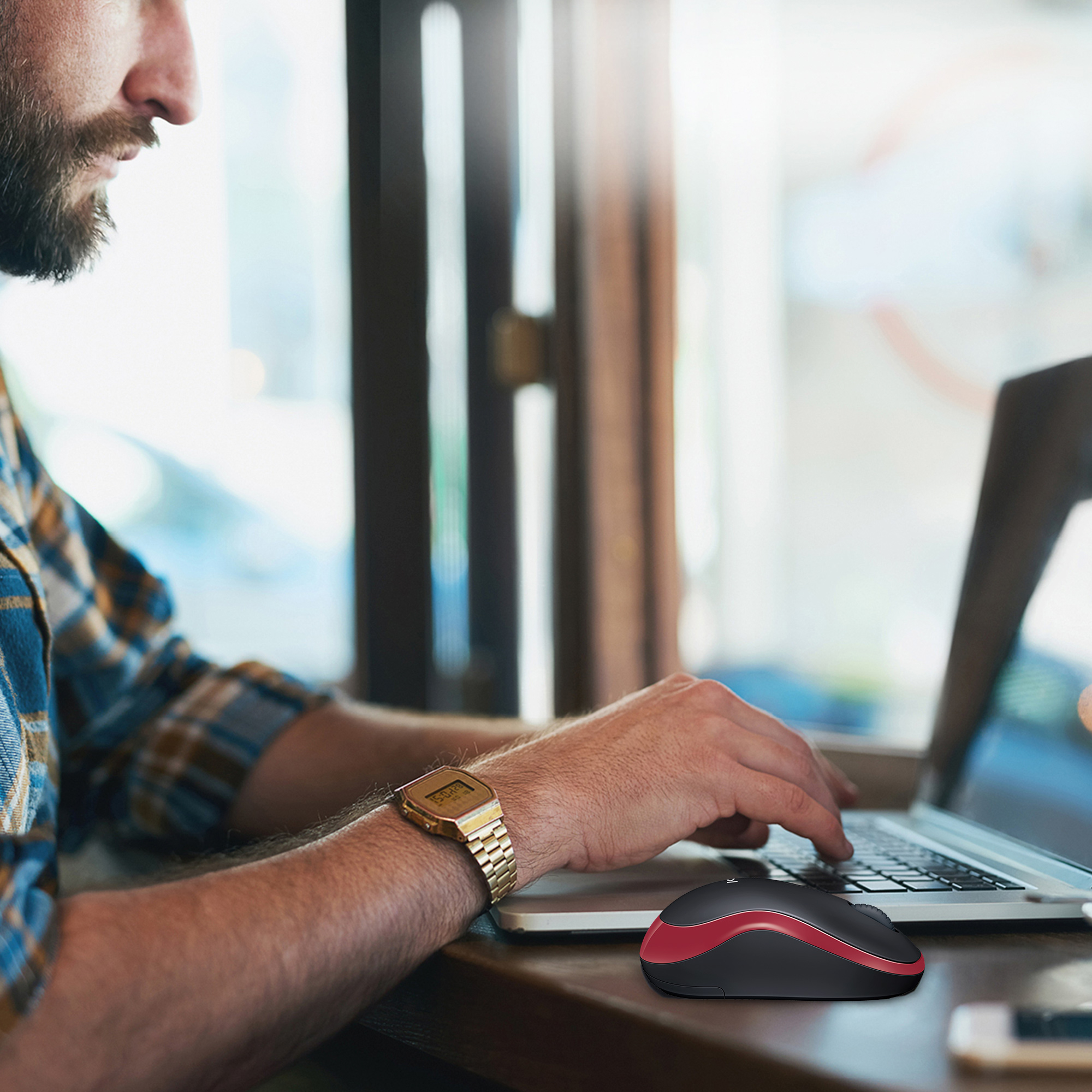 Osoba korzystająca z laptopa, z czerwoną i czarną myszą na stole.