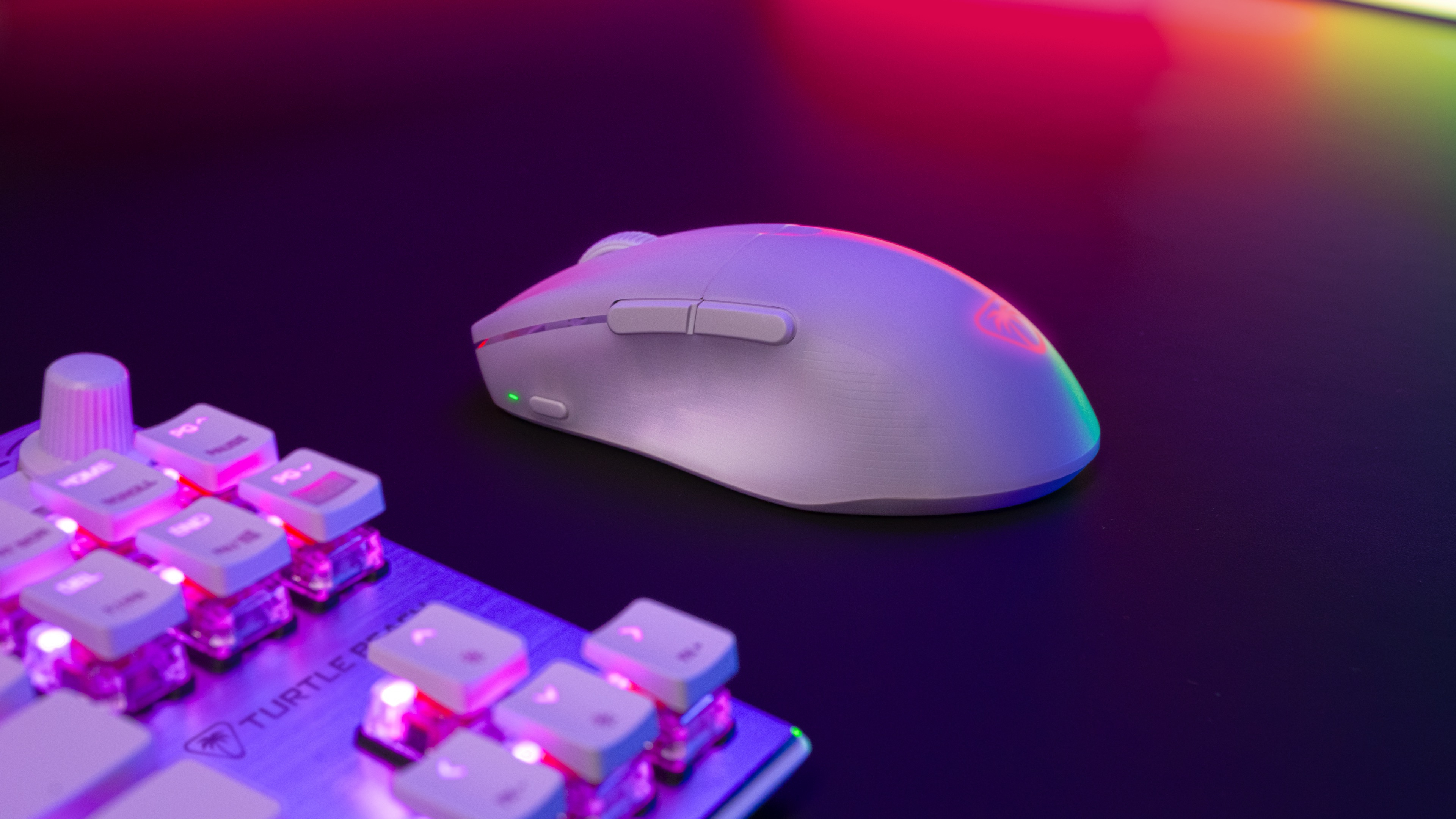 Weiße Gaming-Maus auf einem Schreibtisch mit Tastatur. Bunte Lichter im Hintergrund.