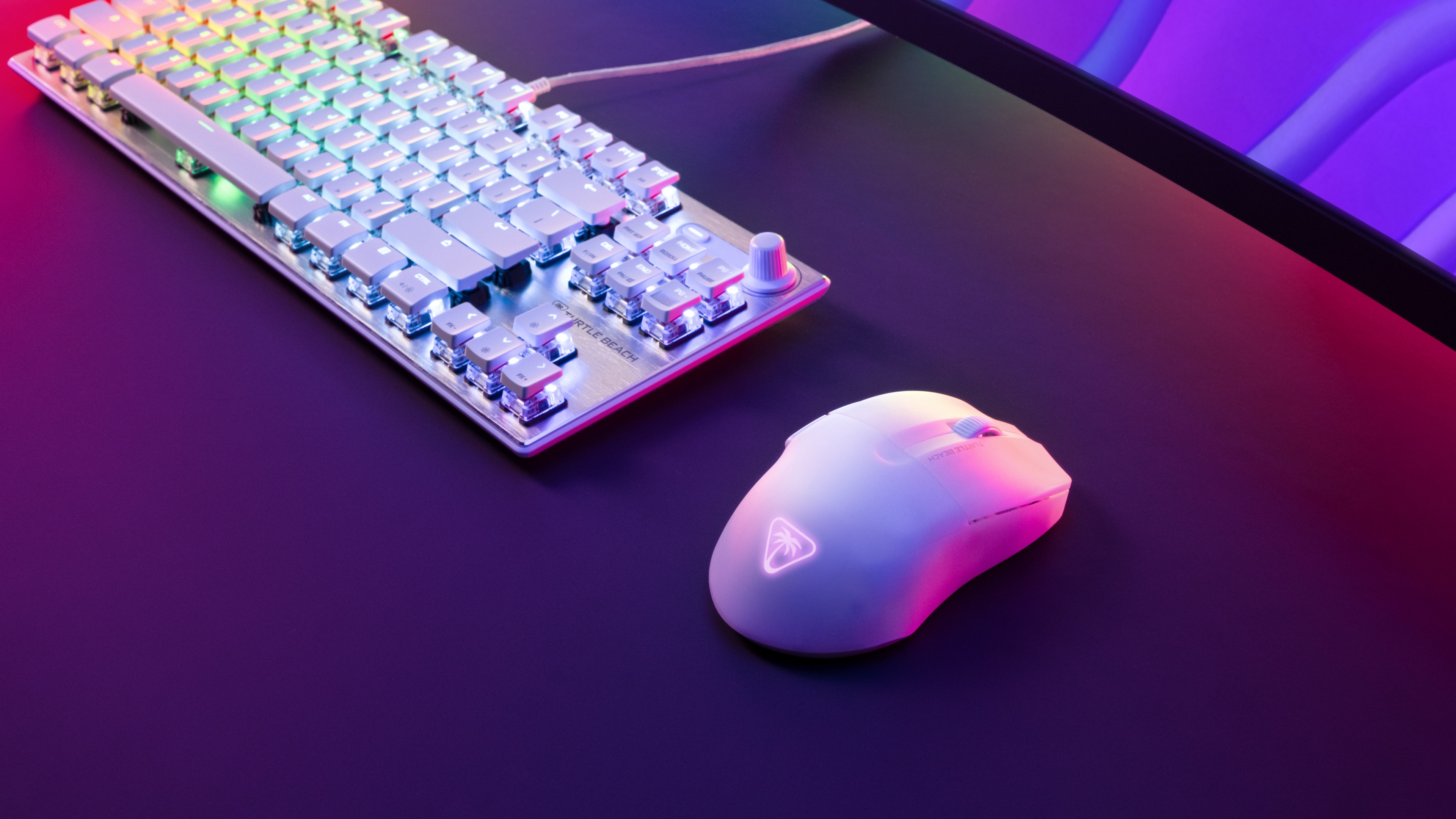 Eine weiße Tastatur und Maus. Die Tastatur leuchtet. Die Maus liegt neben der Tastatur auf einer schwarzen Oberfläche.