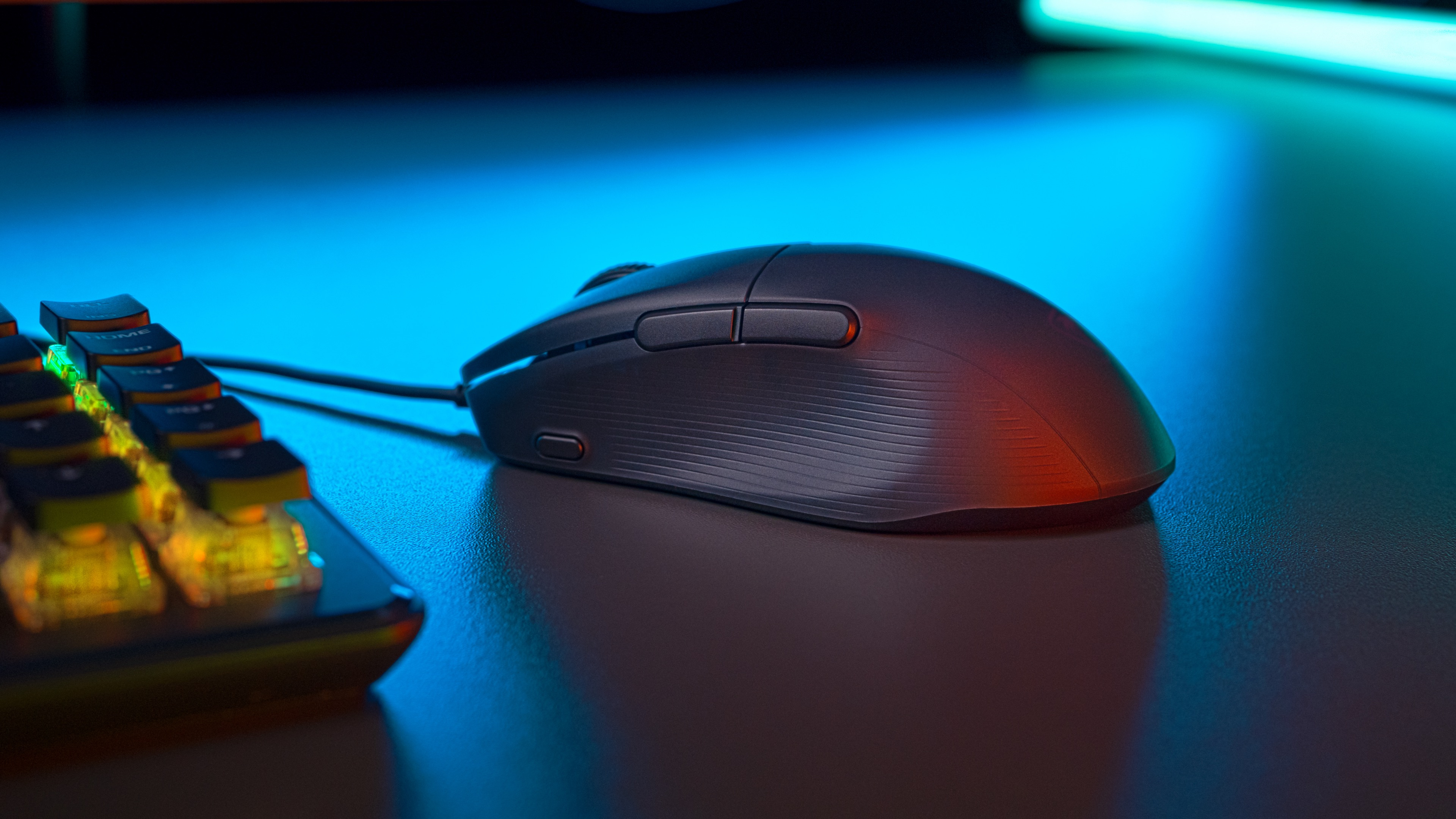 Black gaming mouse with buttons. Near keyboard, under blue and red lighting.