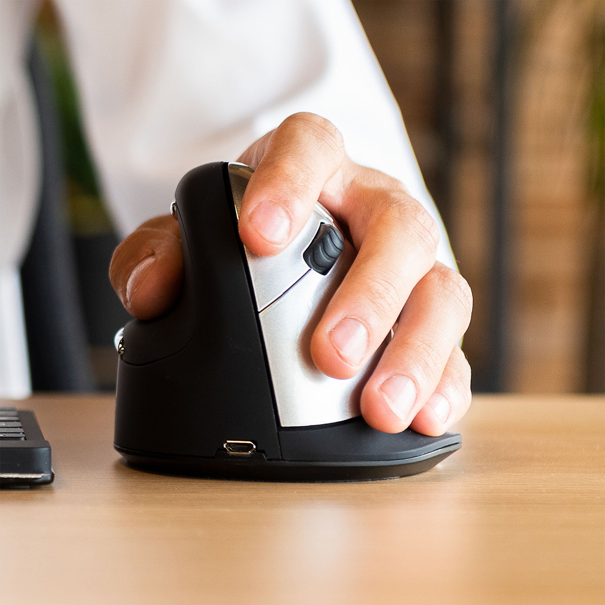Dłoń używająca myszy pionowej. Mysz jest czarna i srebrna.