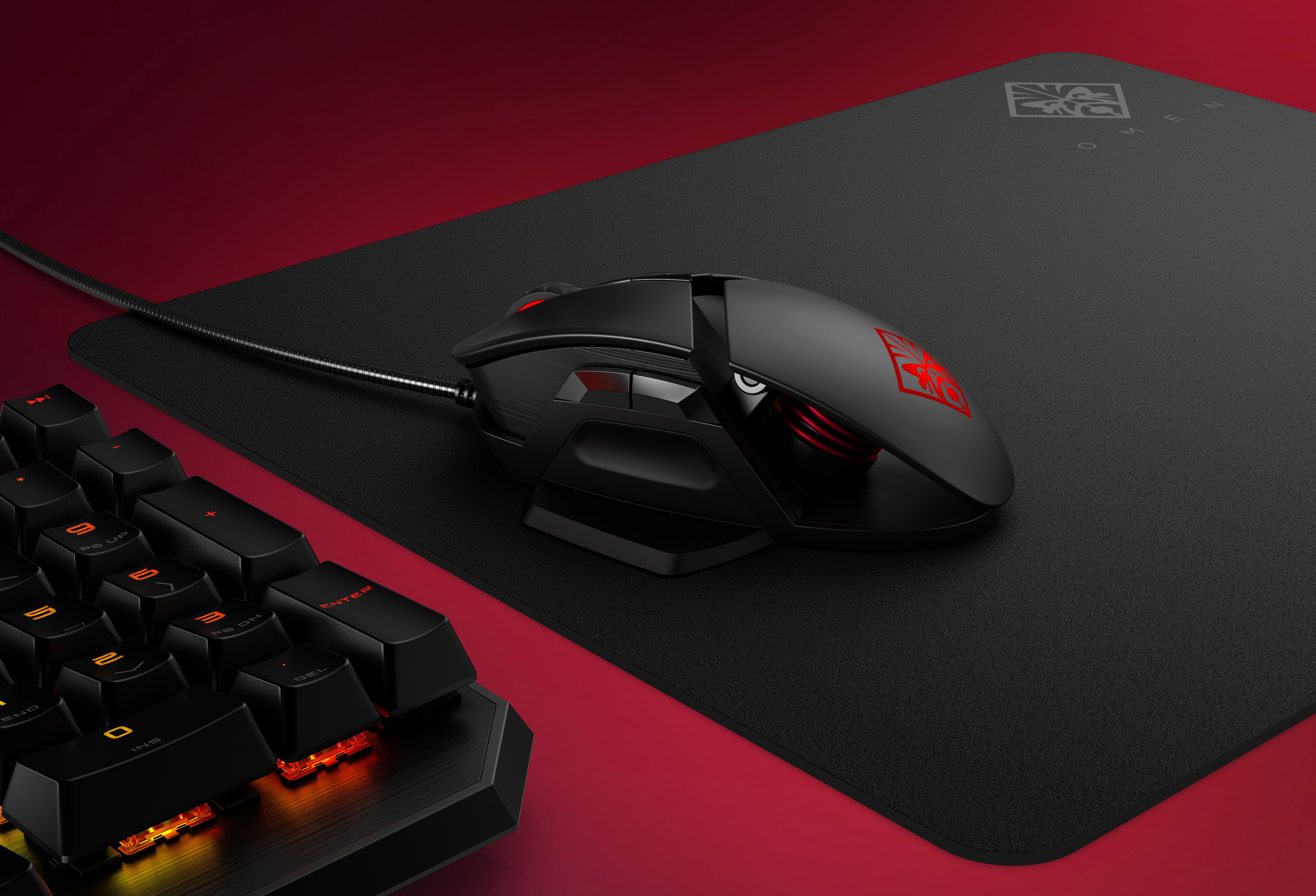 Czarna mysz do gier na czarnej podkładce z klawiaturą. Czerwono-czarna kolorystyka.