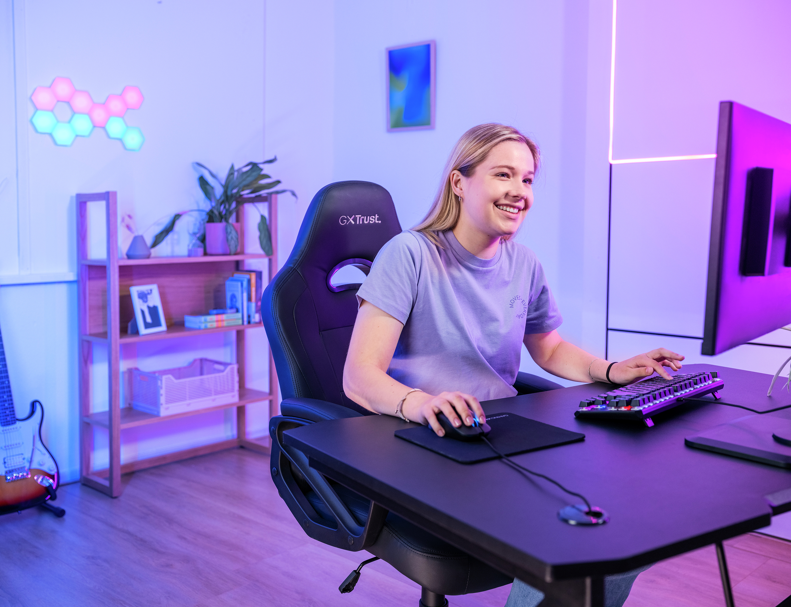 A woman smiling while using a computer, with a gaming chair and monitor.