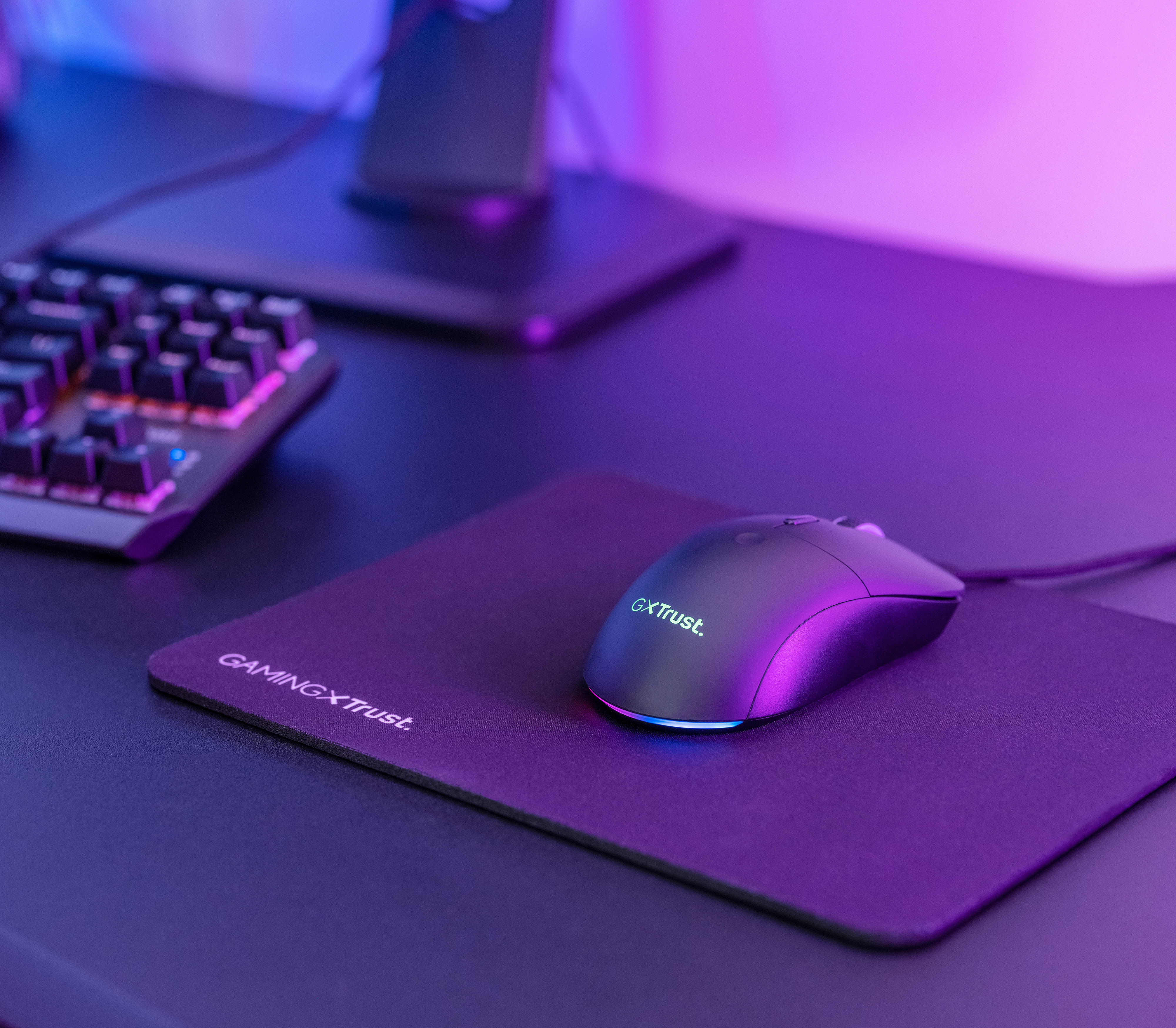 A gaming mouse and mousepad on a black desk. Keyboard and monitor are in the background.