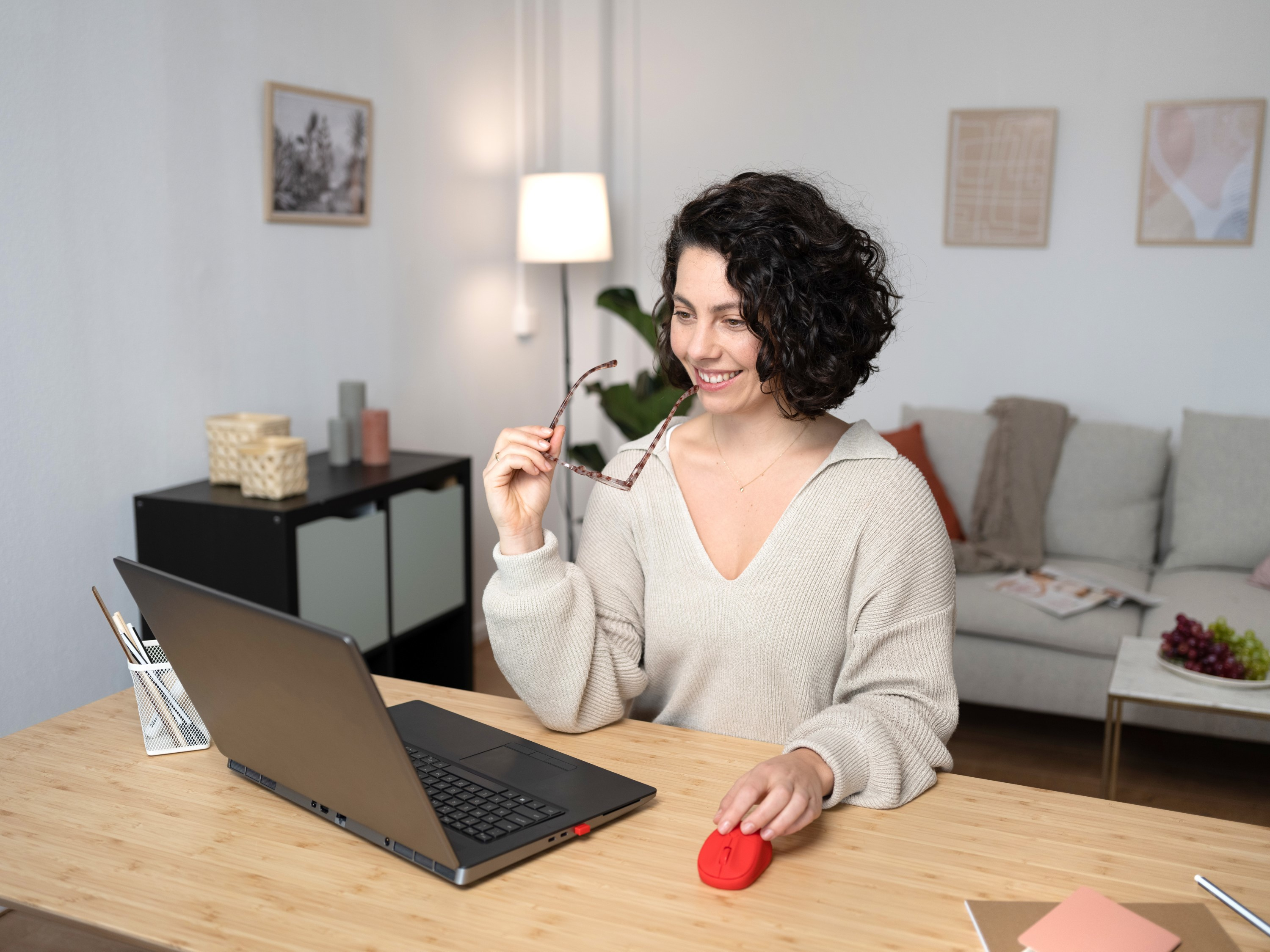 Una donna usa un laptop e un mouse rosso. Un tavolo con una lampada e altri oggetti è sullo sfondo.