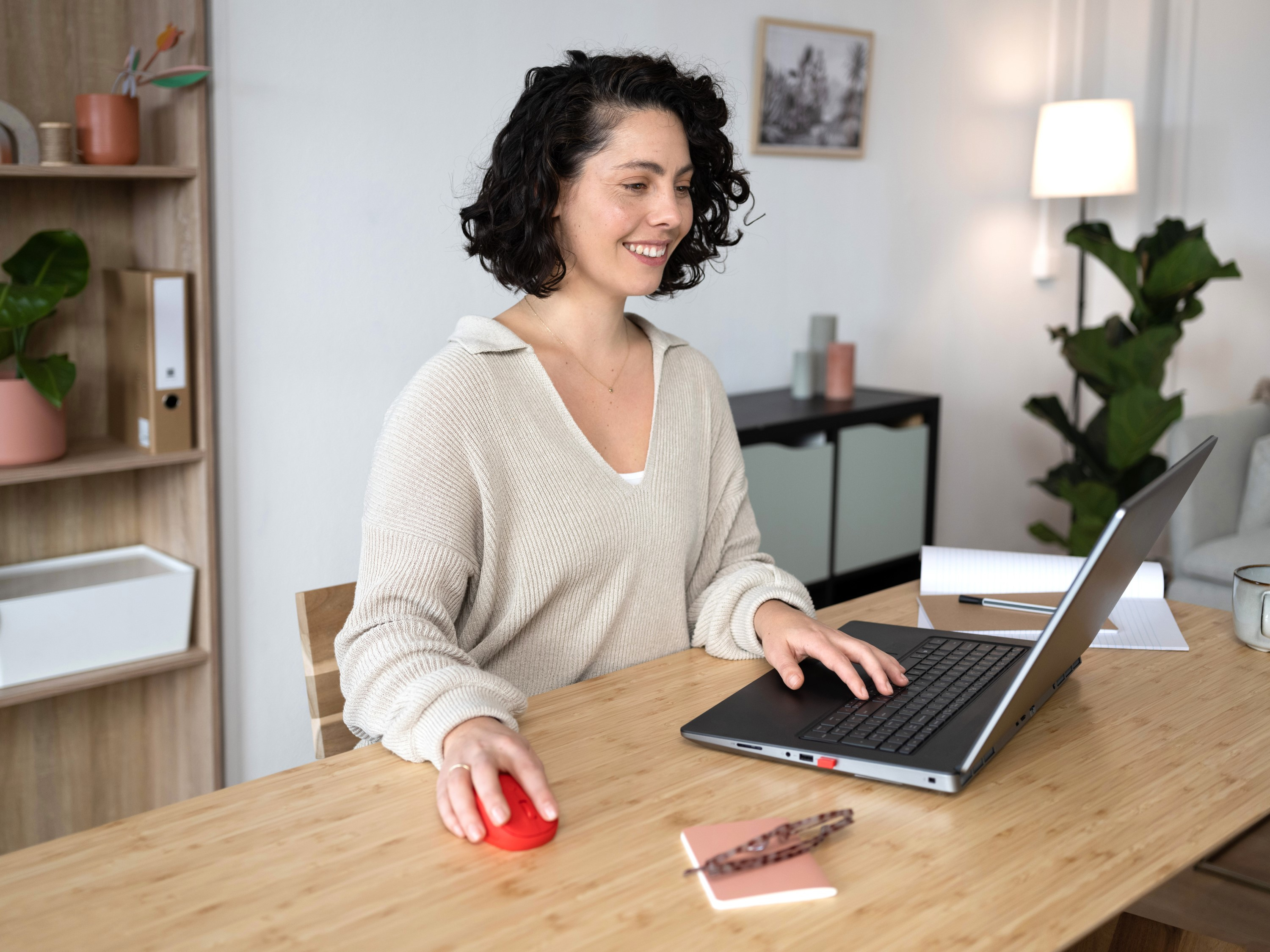 Donna che usa un laptop e un mouse rosso su una scrivania di legno.