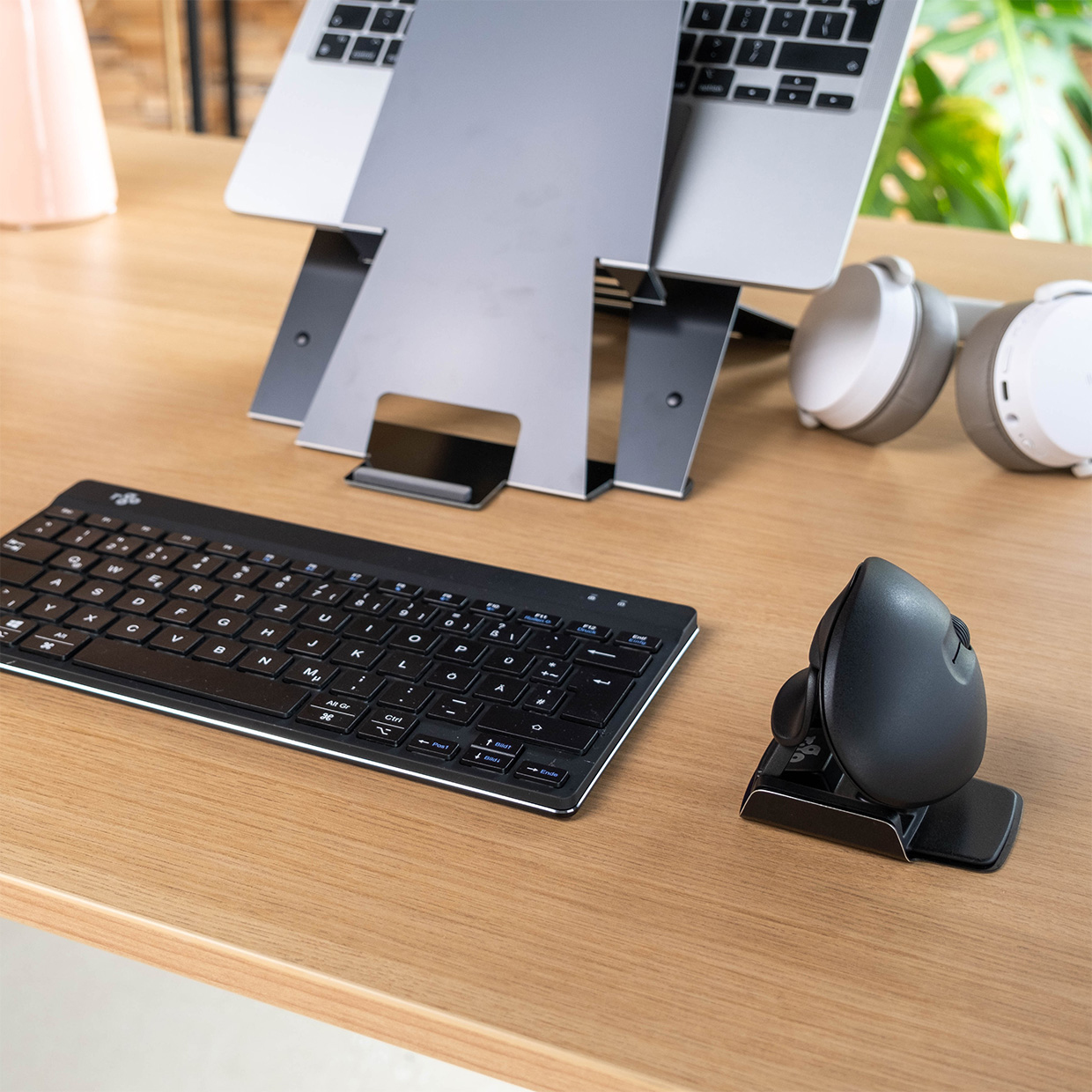Een bureau-opstelling met een laptopstandaard, draadloos toetsenbord, muis en koptelefoon.